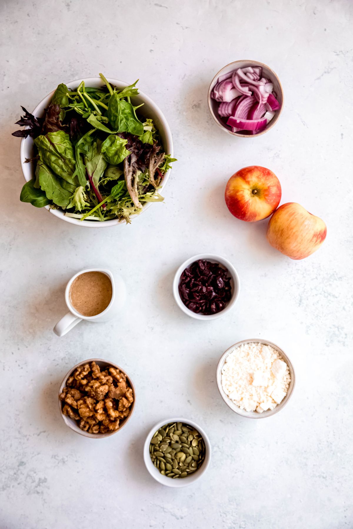 ingredients needed to make an apple & walnut salad recipe measured out on a white table.