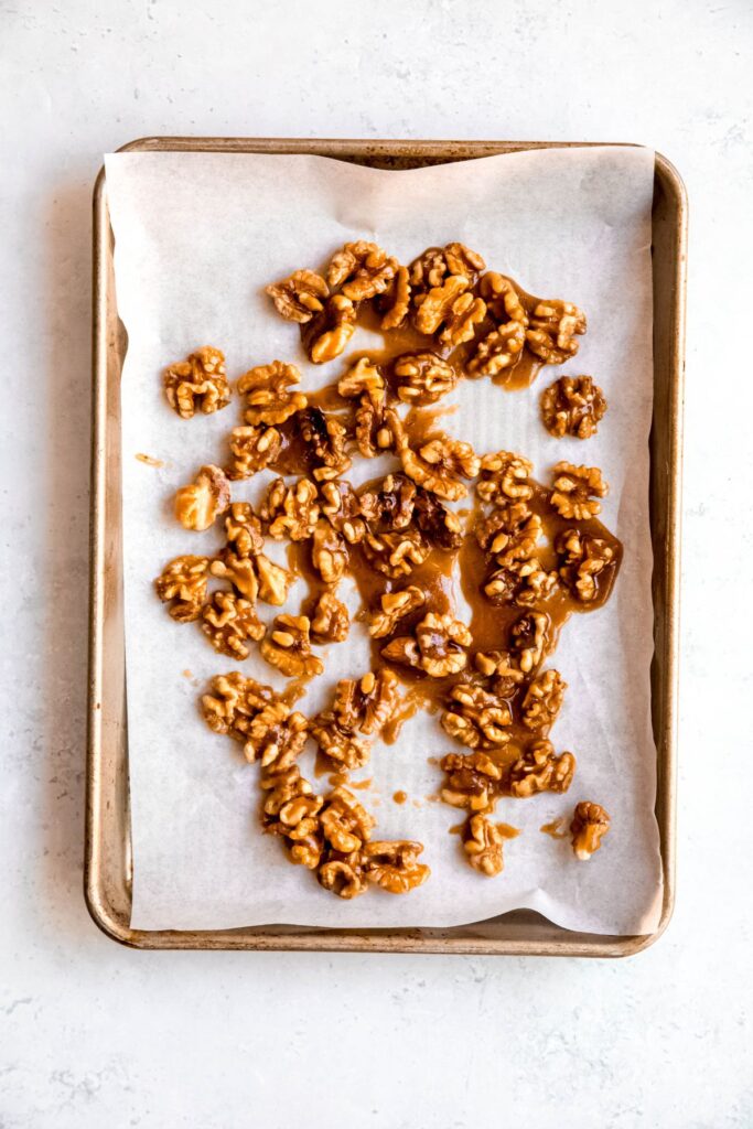 candied walnuts spread out on a parchment lined baking sheet.