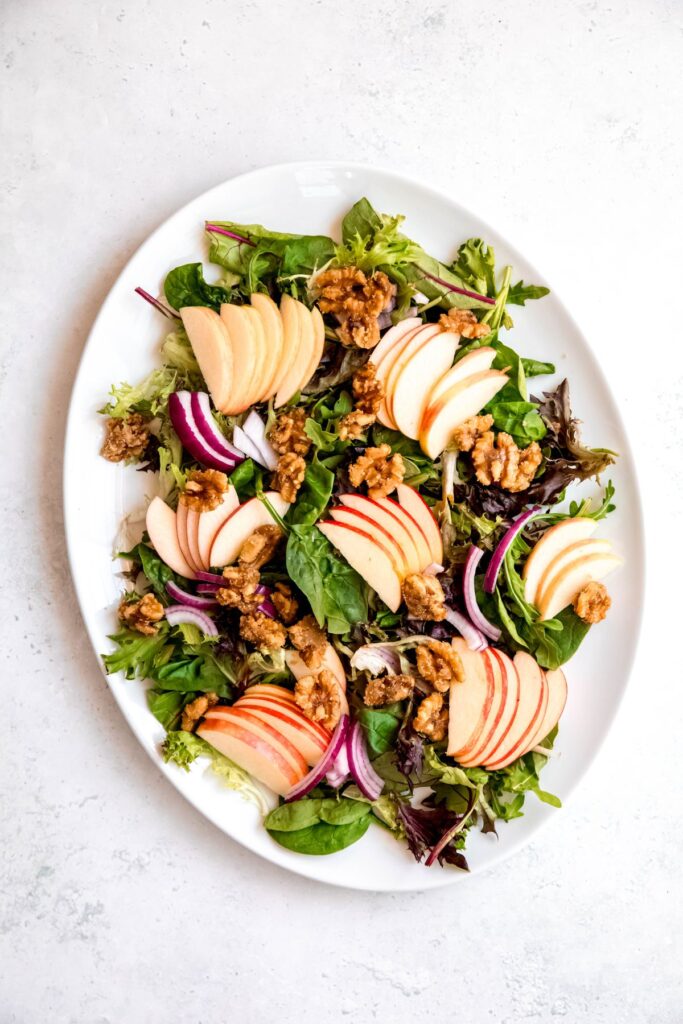 oval serving platter topped with mixed greens, sliced apples, sliced red onions, and candied walnuts.