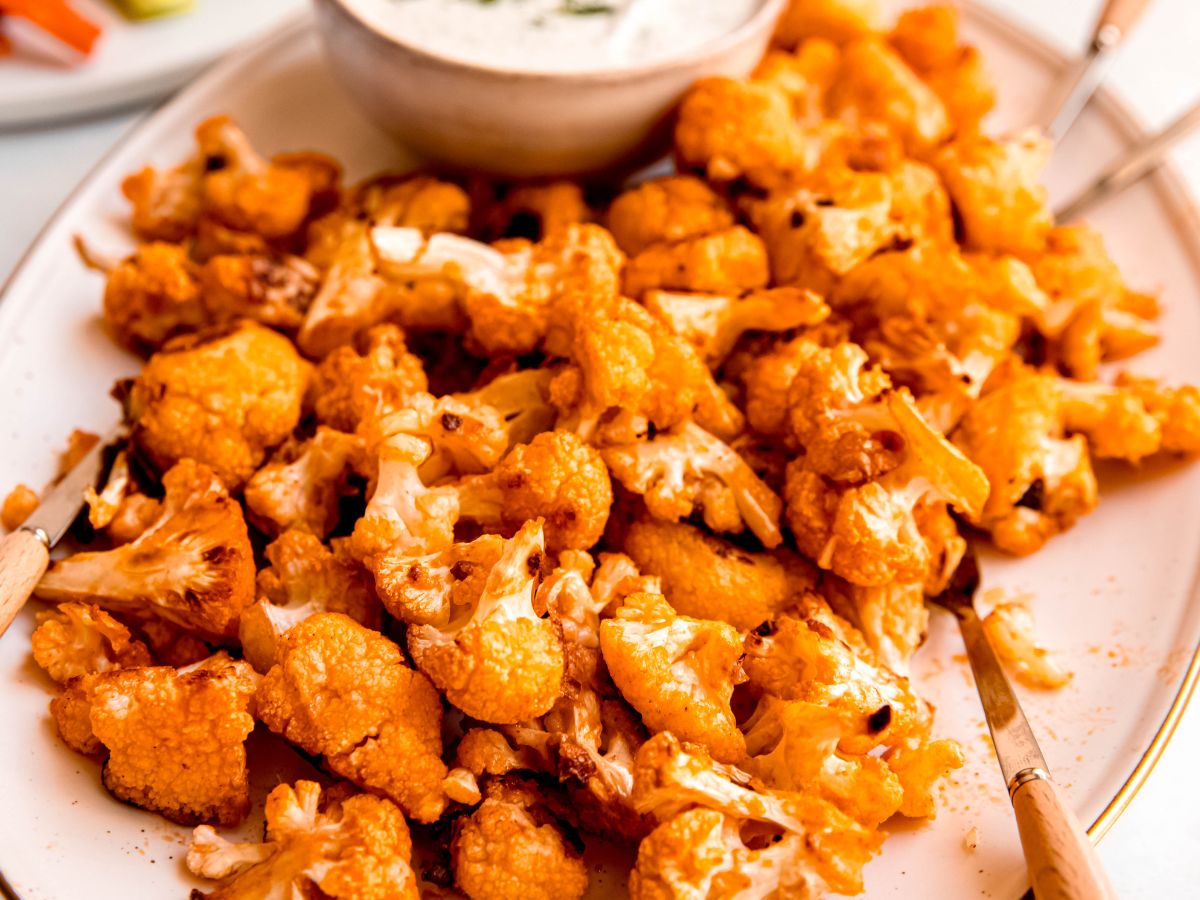 square closeup hero shot of buffalo cauliflower bites speared with 4 silver and pale wood appetizer forks.