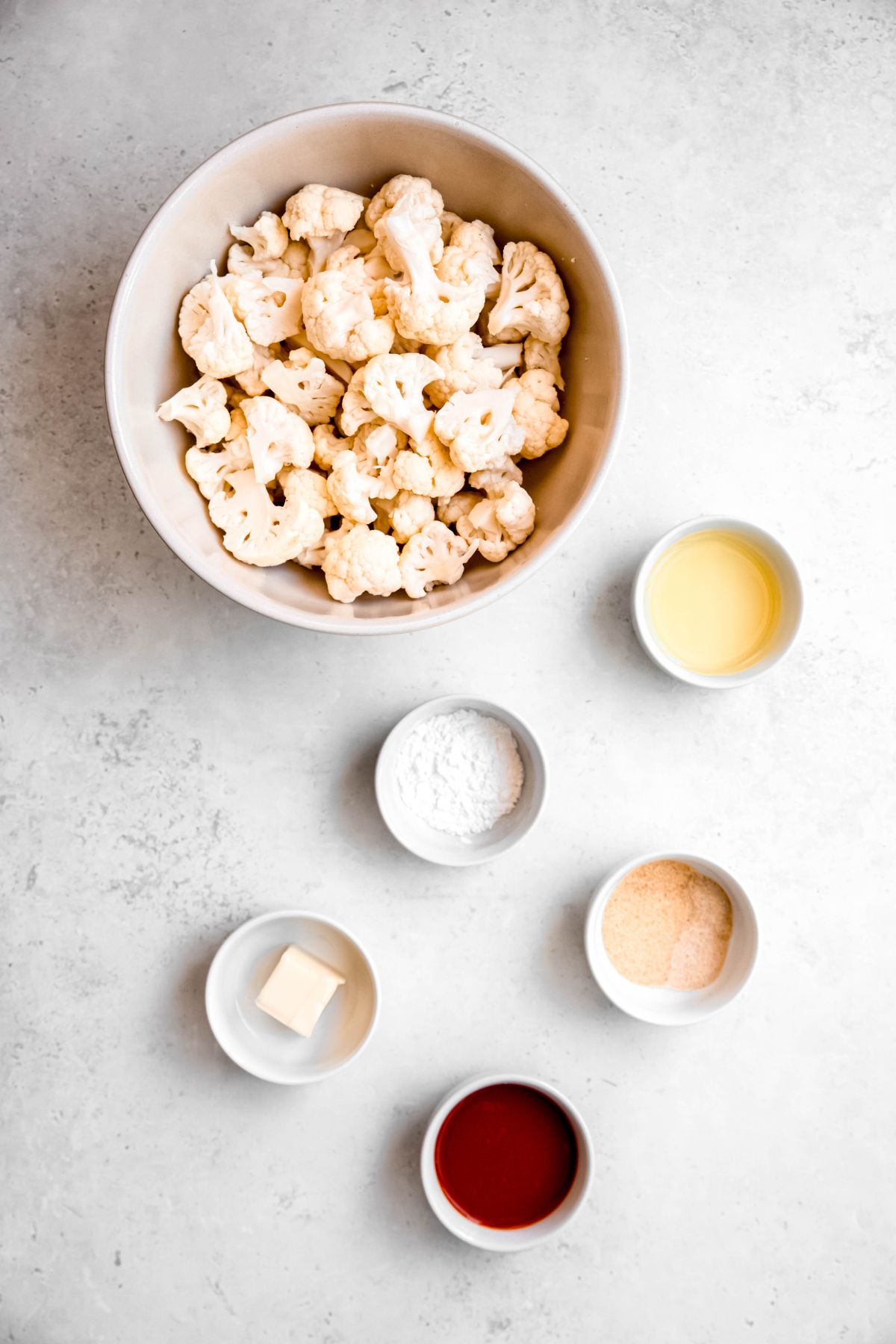 ingredients for making crispy oven baked buffalo cauliflower wings measured out in white bowls on a white table.