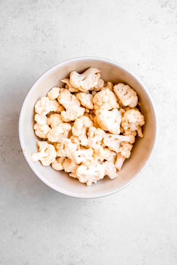 cauliflower florets in a mixing bowl after tossing with avocado oil, seasoning, and cornstarch.