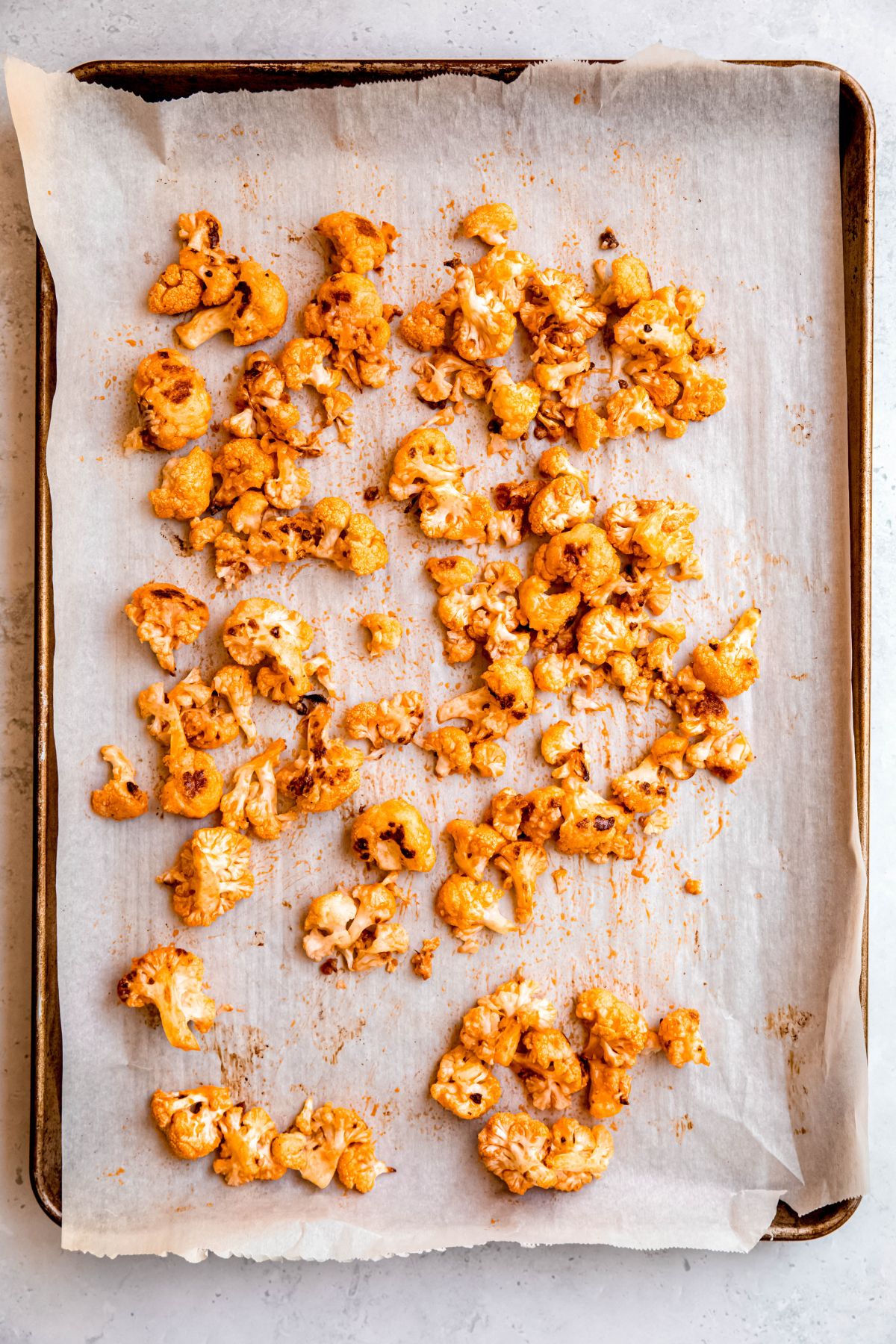 buffalo roasted cauliflower bites on a parchment lined sheet pan after tossing in the wing sauce and baking a second time.
