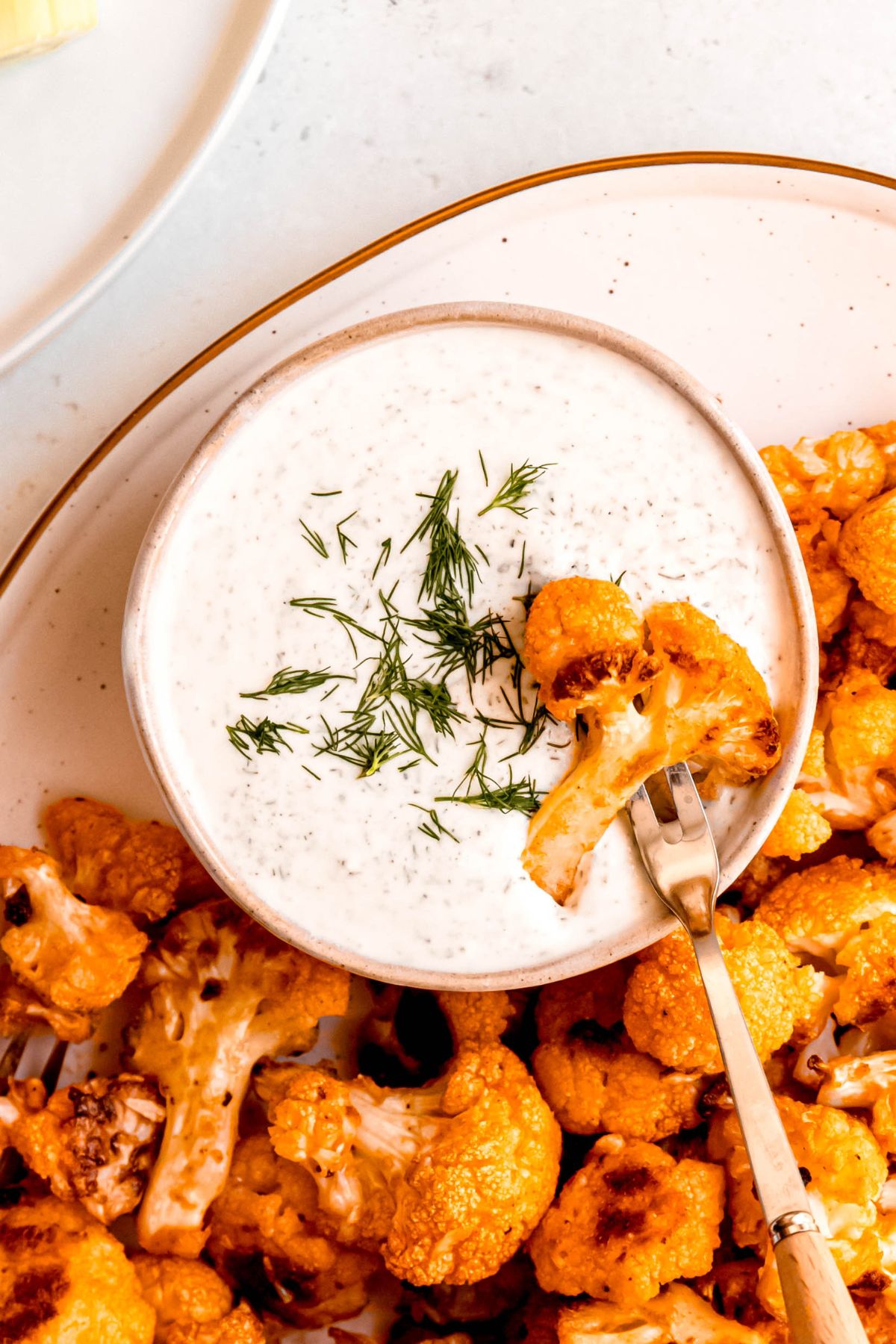 closeup shot of a single oven roasted buffalo cauliflower bite on a silver oyster fork being dipped into the ranch dressing.