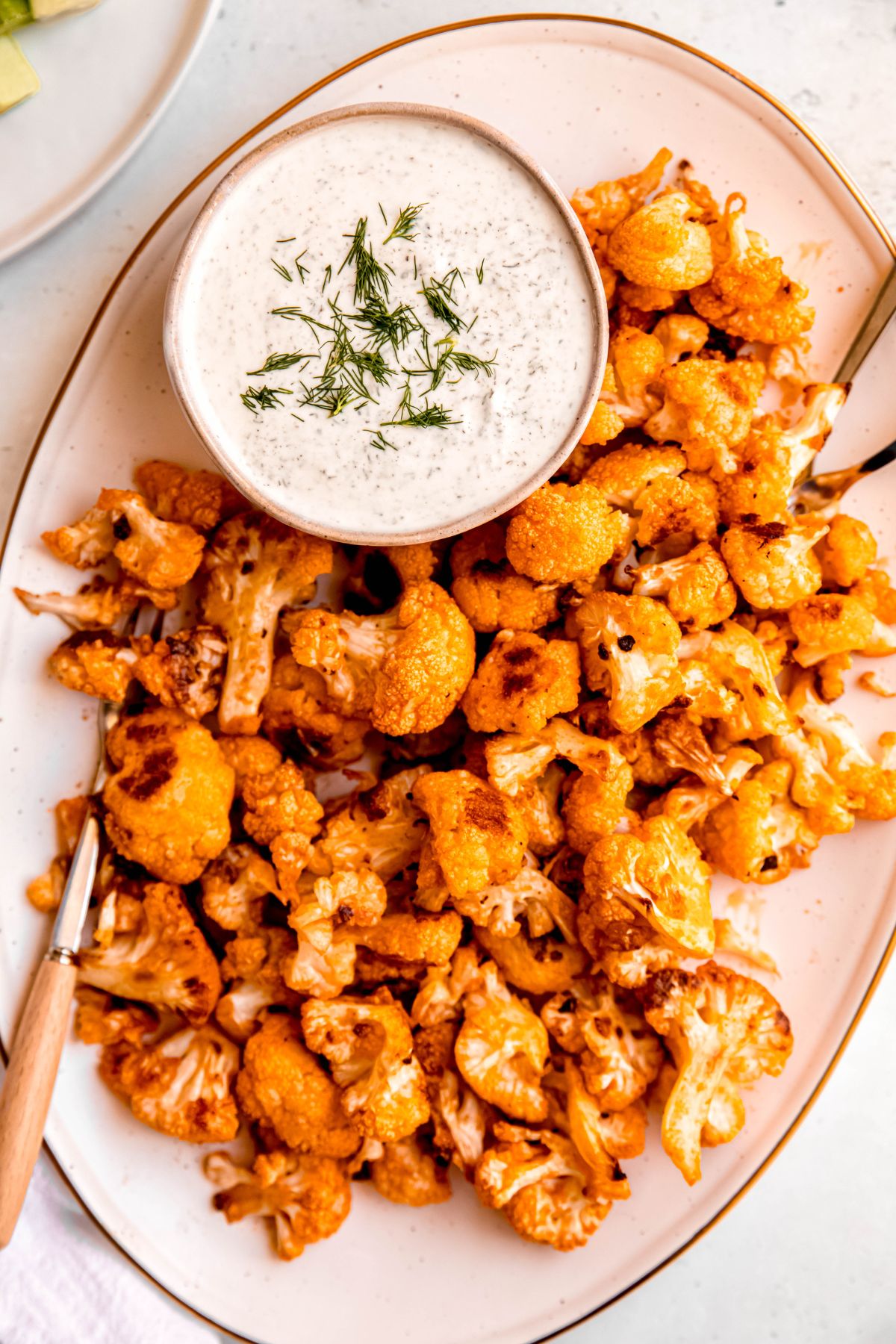 white oval serving platter filled with roasted buffalo cauliflower wings served with a dill-garnished bowl of ranch dressing.