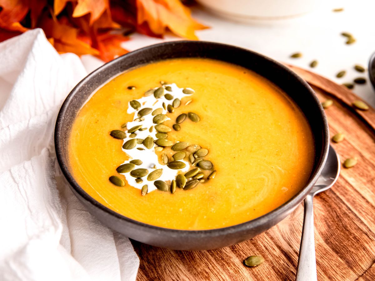 final 45 degree angle horizontal hero shot of one pot, creamy, high protein butternut squash and apple soup garnished with a drizzle of cream and a sprinkle of pepitas for garnish.