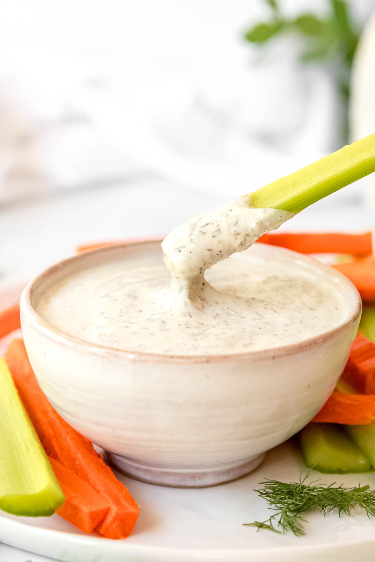 A close-up shot of a piece of celery dipped into a small bowl of Greek yogurt ranch dressing.