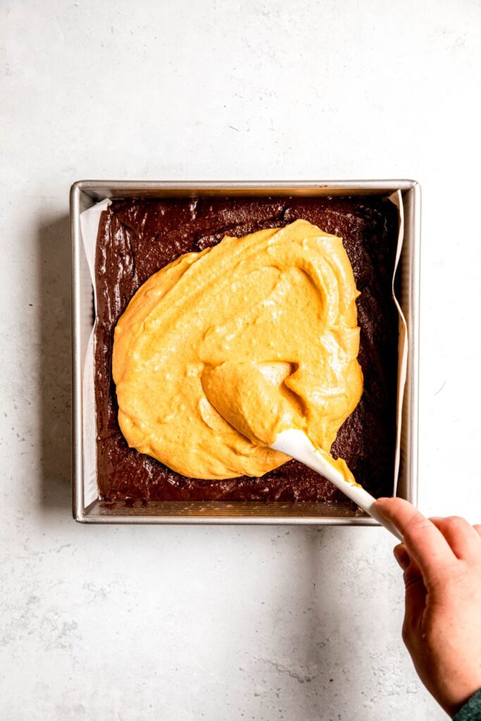 Spreading the pumpkin cheesecake batter on top of the brownie batter layer.