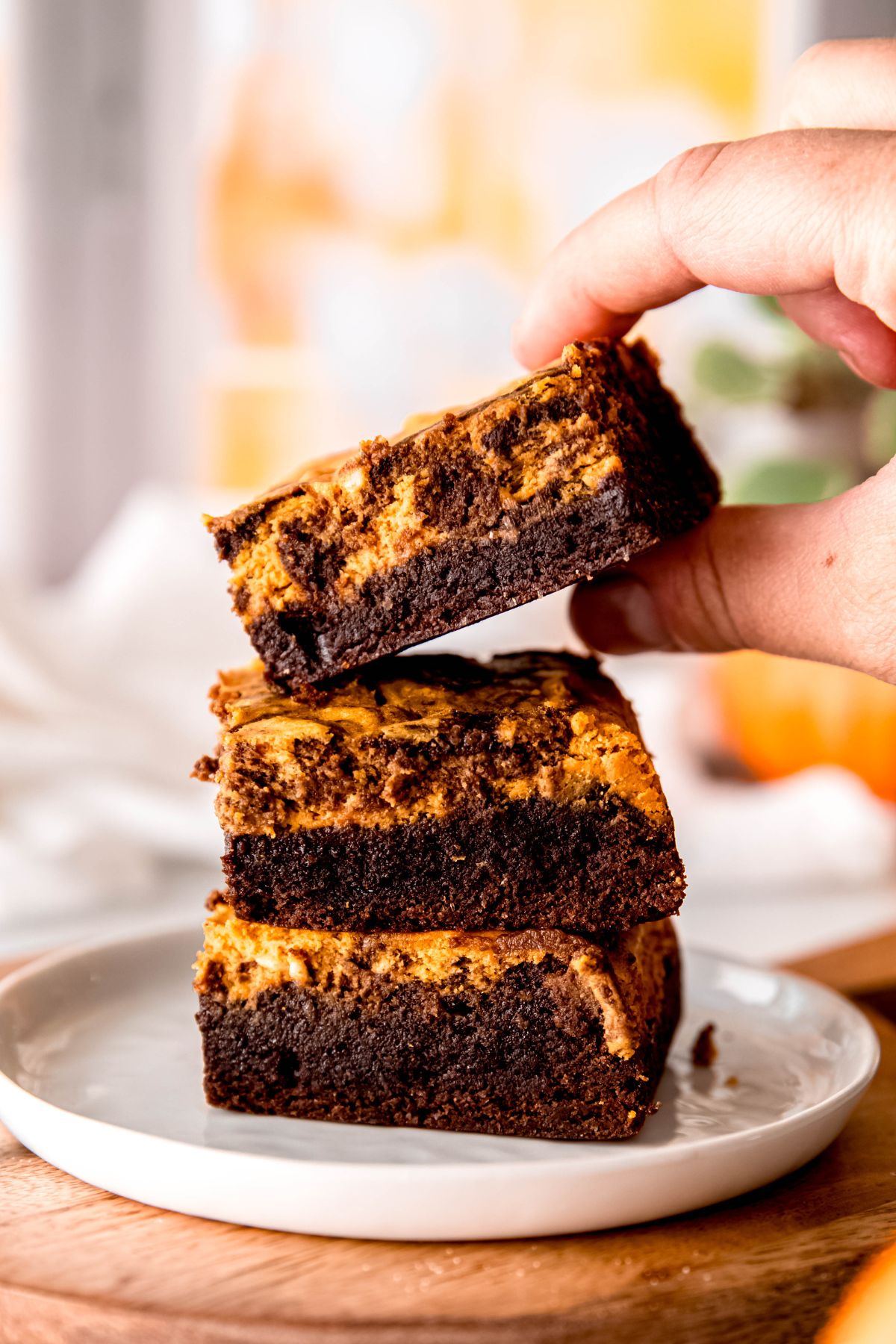 A hand picking a pumpkin brownie off a stack on a plate.