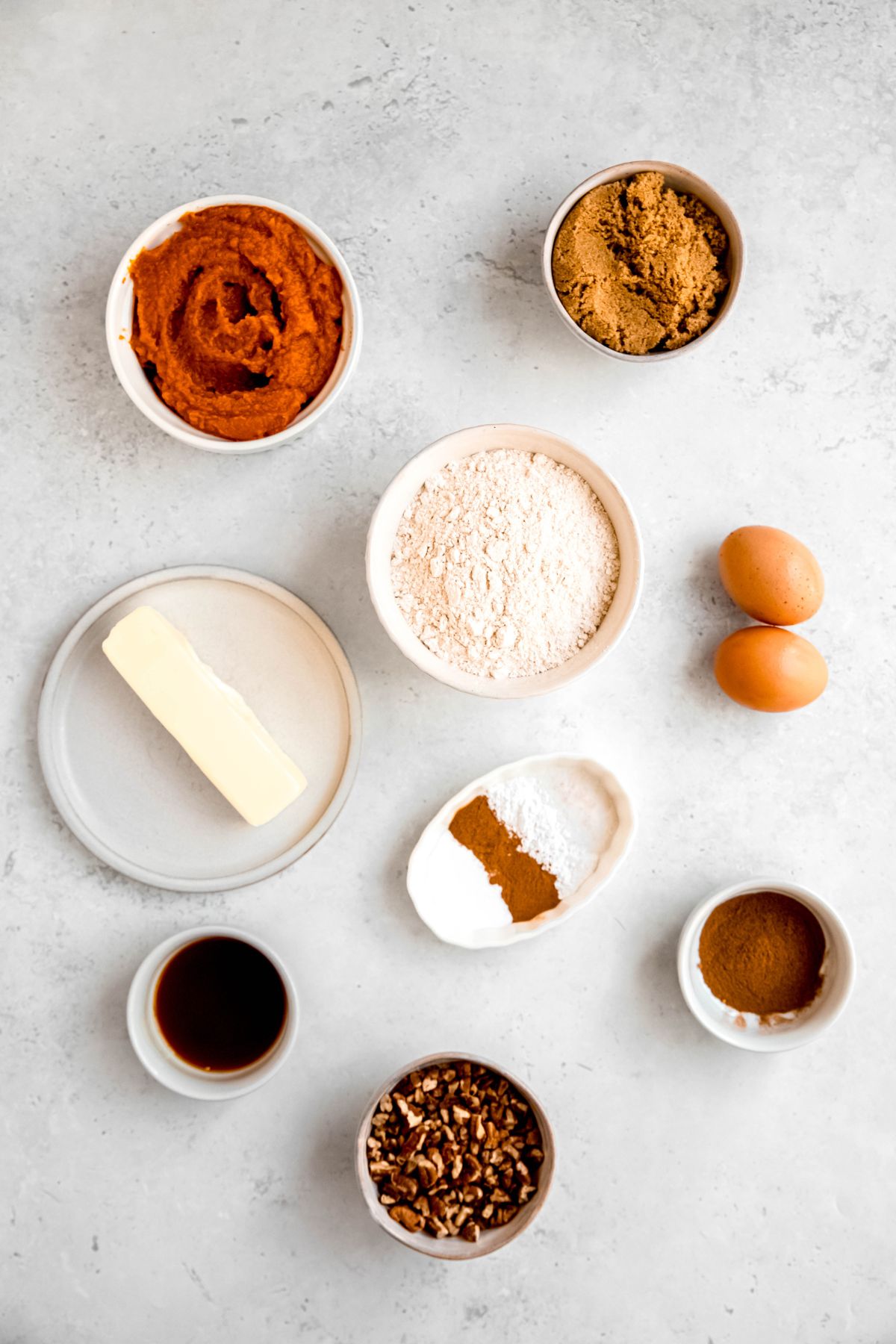 ingredients to make pumpkin crumble bars recipe measured out into bowls on a white table.