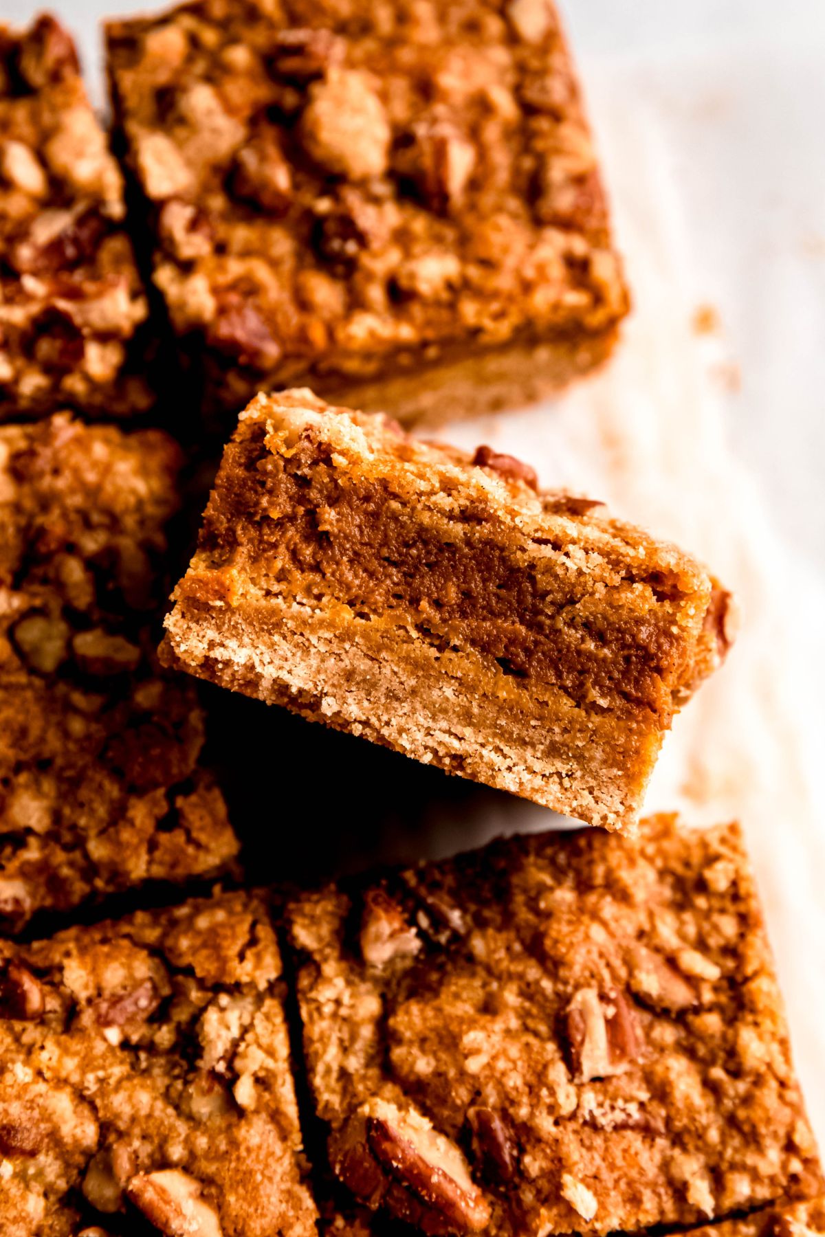 closeup on a batch of freshly cut pumpkin crumb bars on a parchment paper sling with one turned on its side towards the camera to show the distinct layers.