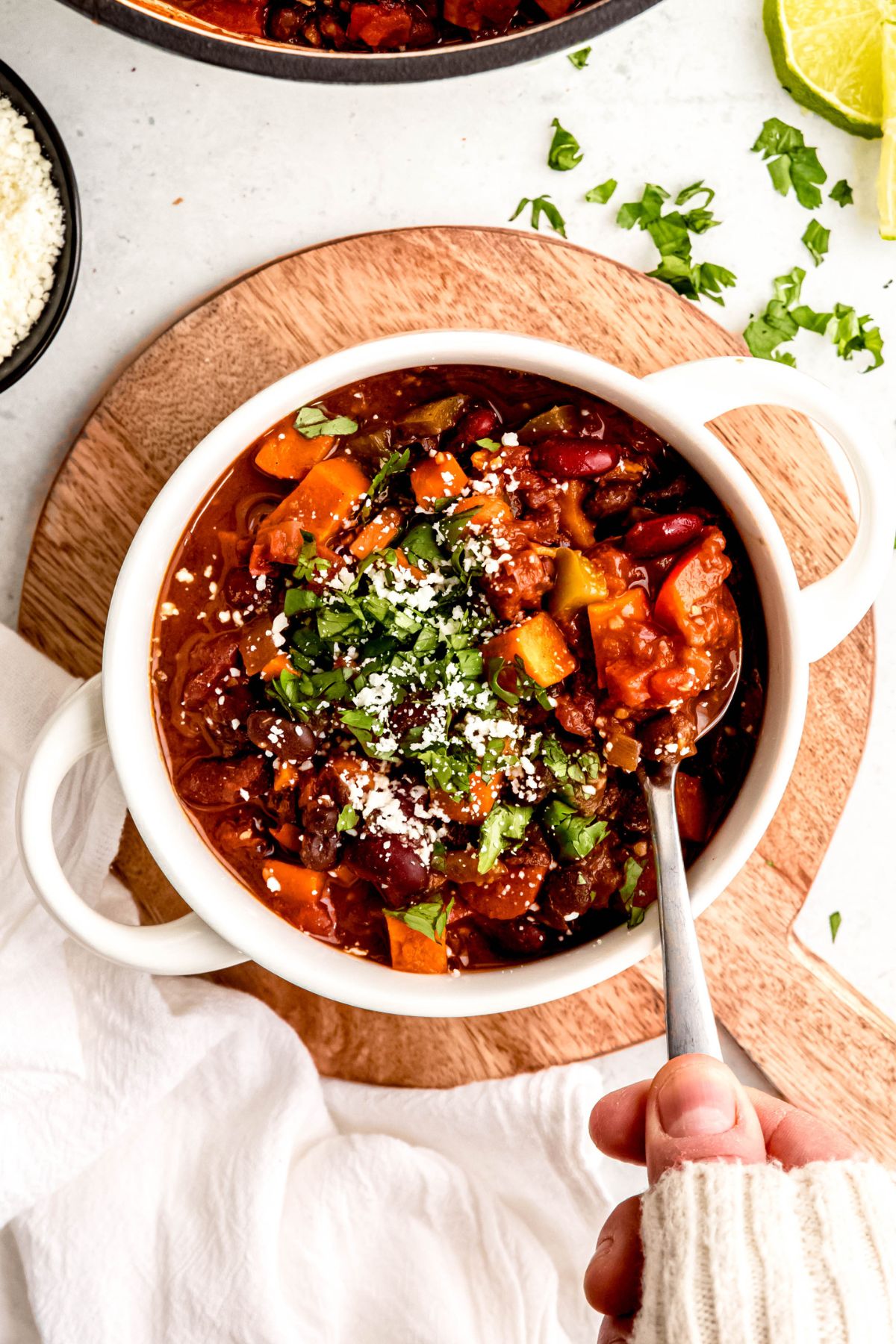 An overhead shot of a hand taking a large scoop of sweet potato chili.