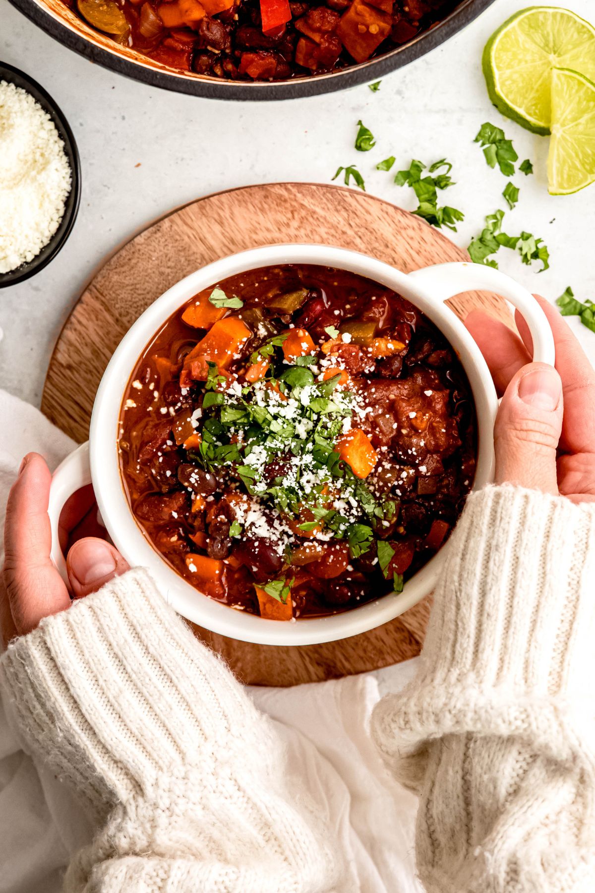 An overhead shot of a crock of sweet potato vegetarian chili with two hands holding the crock.