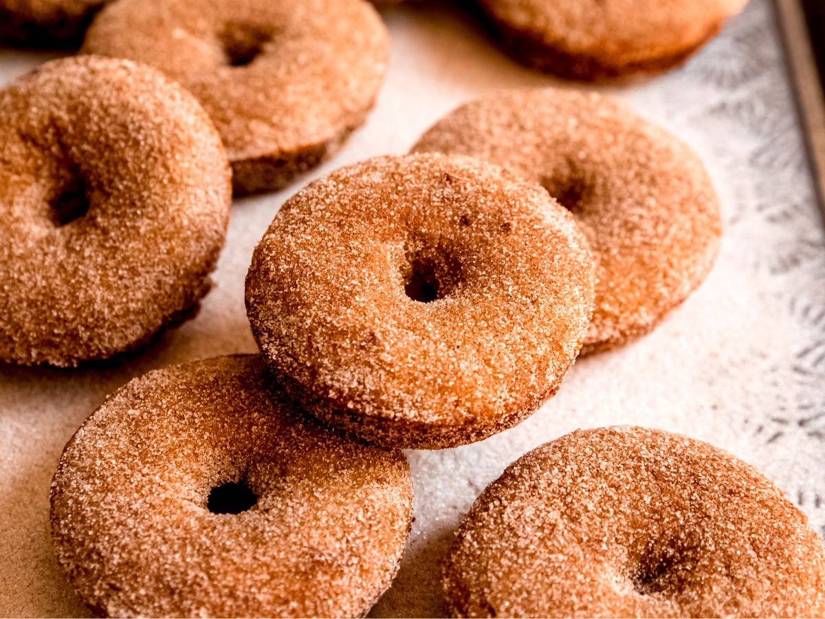 horizontal hero shot of baked apple cider donuts on a sheet pan with cinnamon sugar.