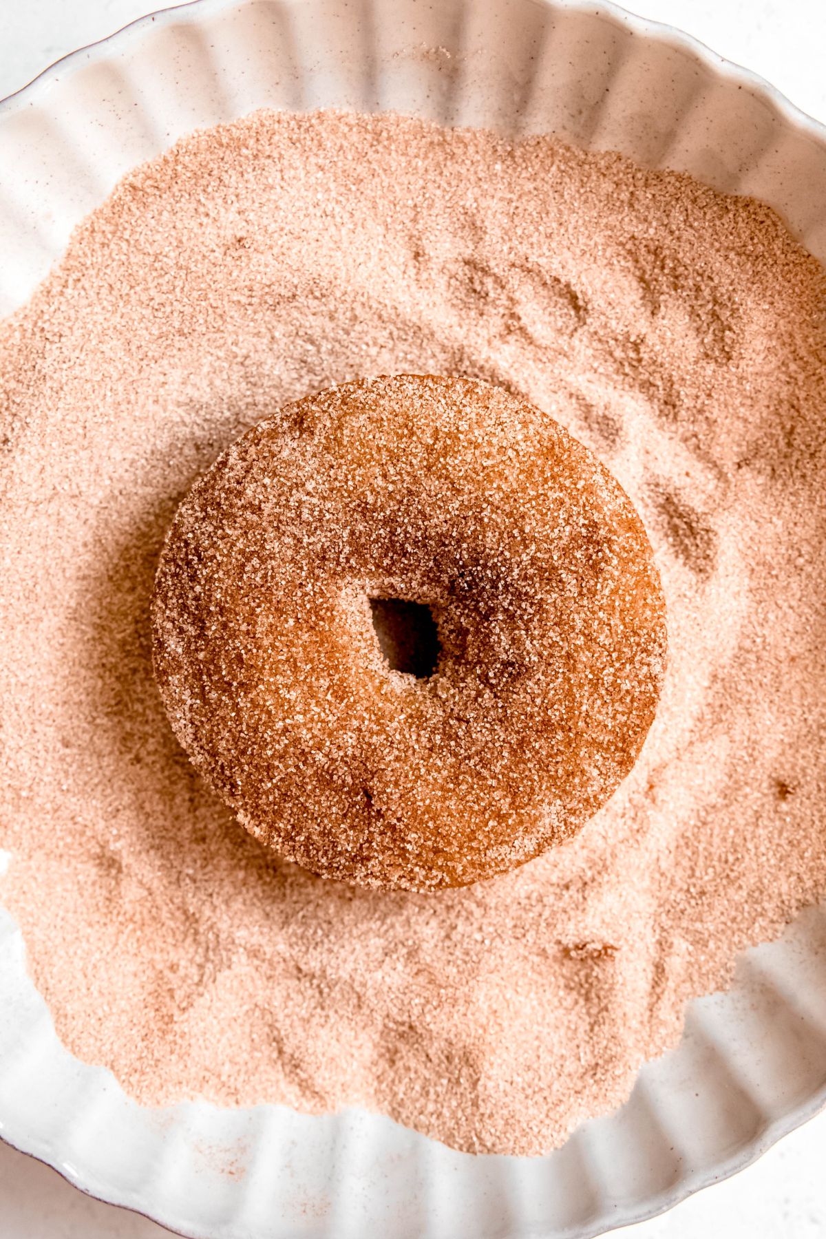 closeup overhead shot of a baked apple cider donut in the cinnamon sugar bowl for coating.