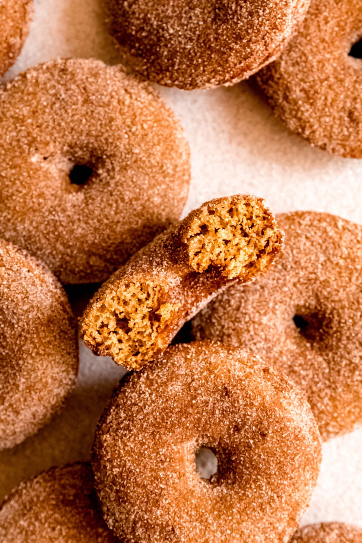 closeup on a halved baked apple donut showing the fluffy cake-like interior with the rest of the jumble of donuts scattered around.