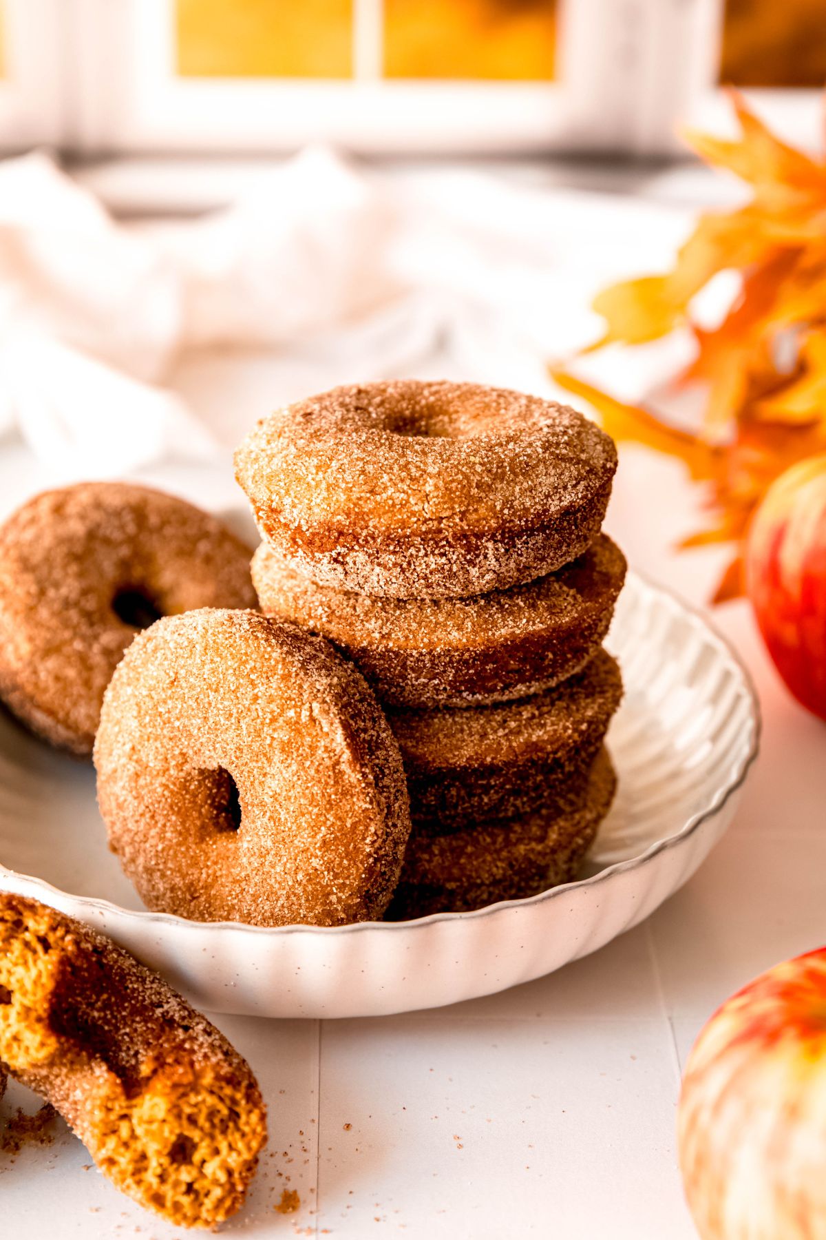 stack of 4 baked cinnamon apple cider doughnuts in a white scalloped pasta bowl with 2 others resting against the tower and the side of the bowl.