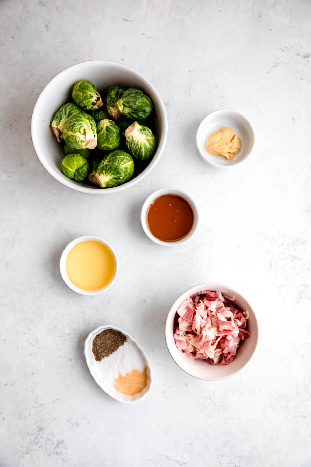 overhead shot of ingredients needed to make caramelized brussels sprouts with bacon and maple dijon glaze measured out on a white table.