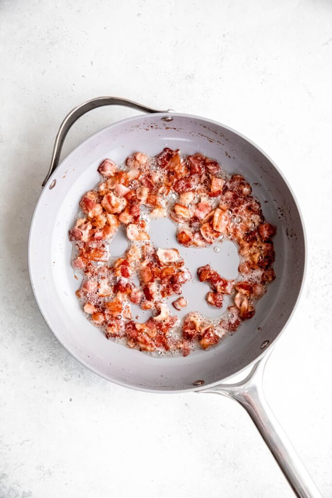 chopped bacon pieces rendering in a skillet.