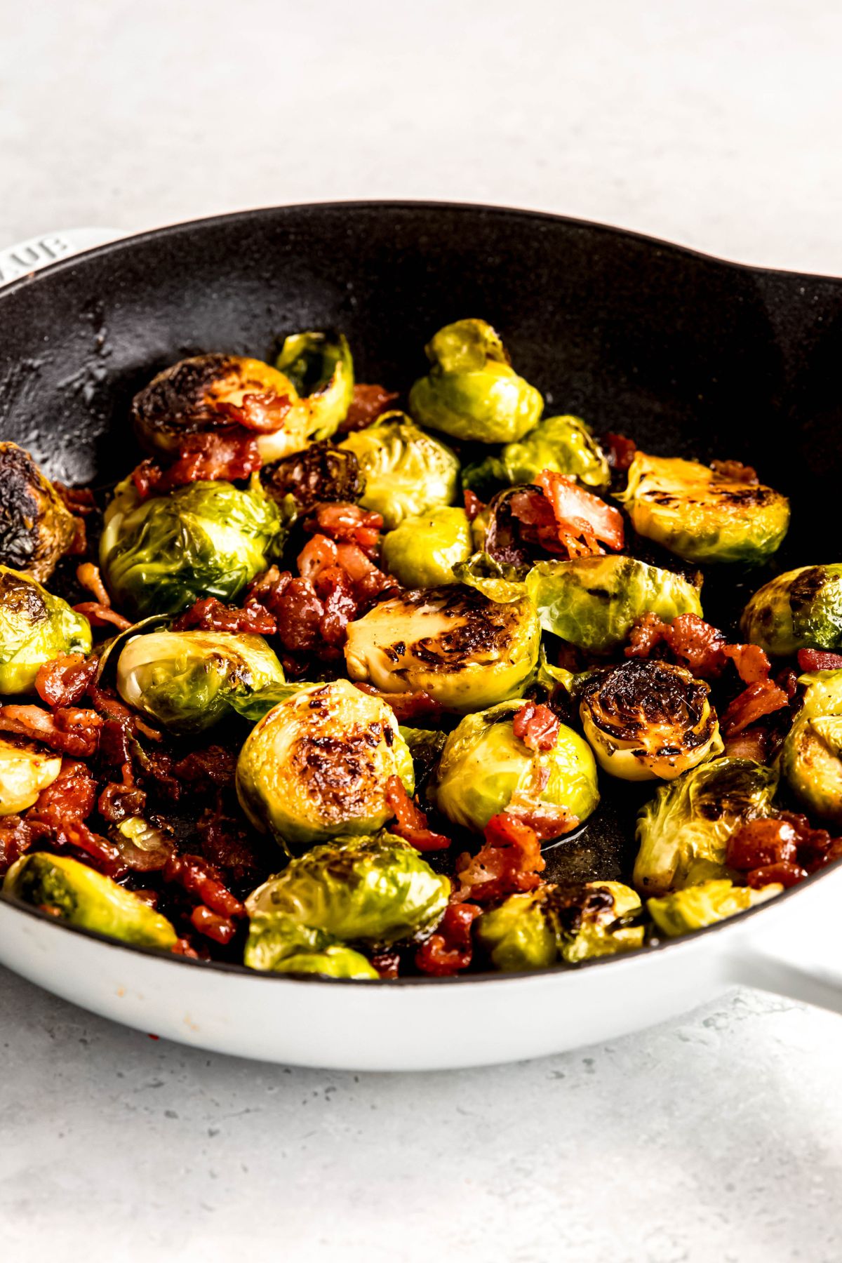 pan roasted brussels sprouts with bacon in a white cast iron skillet.