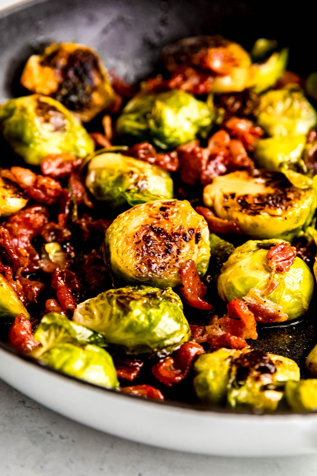 45 degree angle closeup shot of the skillet filled with pan roasted maple dijon brussels sprouts with bacon bits.