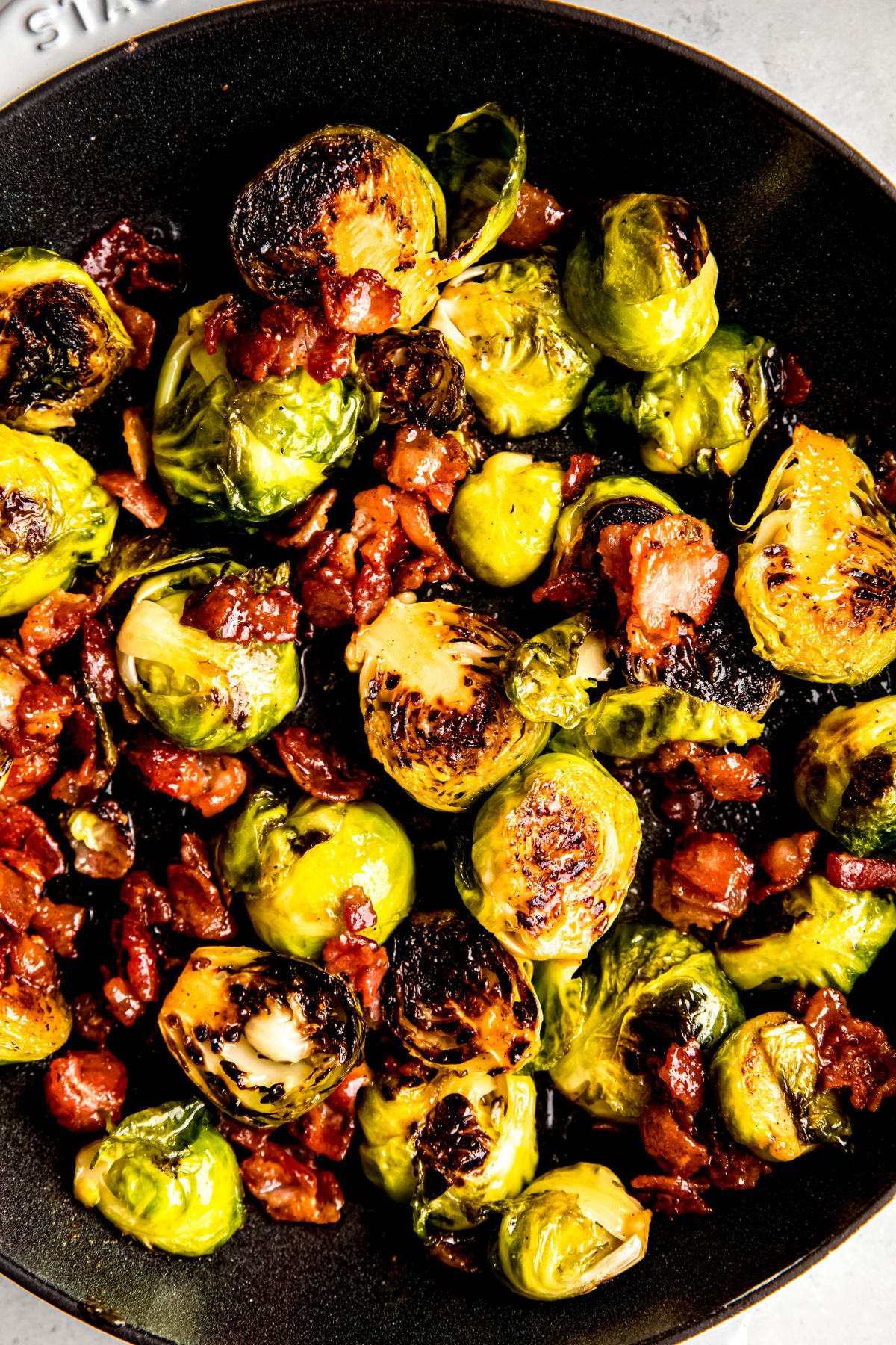 closeup overhead shot of caramelized brussel sprouts with bacon bits tossed in a maple dijon sauce serving in a black bowl.