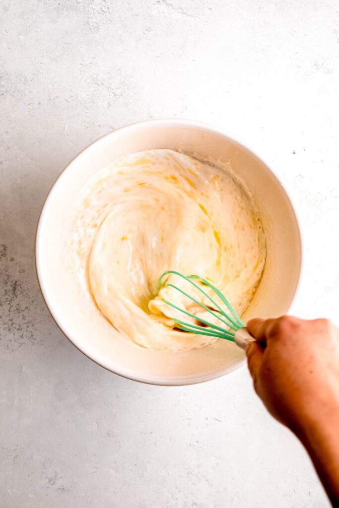 A hand whisking the wet ingredients for the cornbread topping.