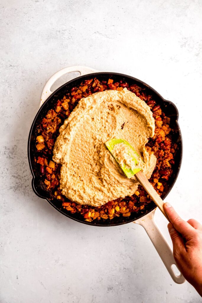 How to make chili cornbread casserole: a hand spreading the cornbread mixture on the casserole before baking.