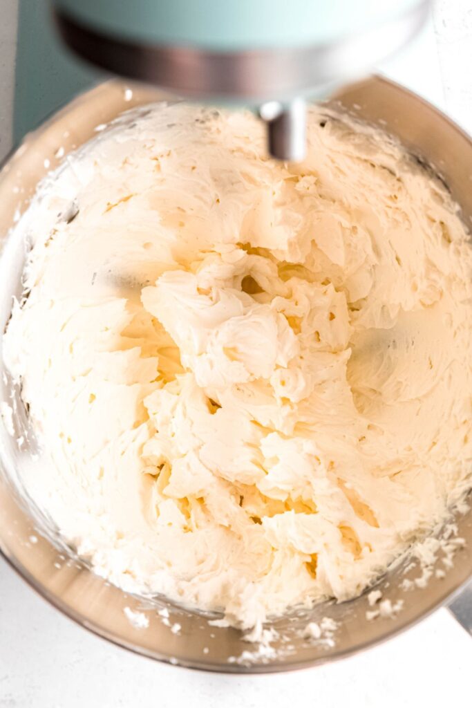 whipped cream cheese in a metal mixing bowl on a stand mixer.