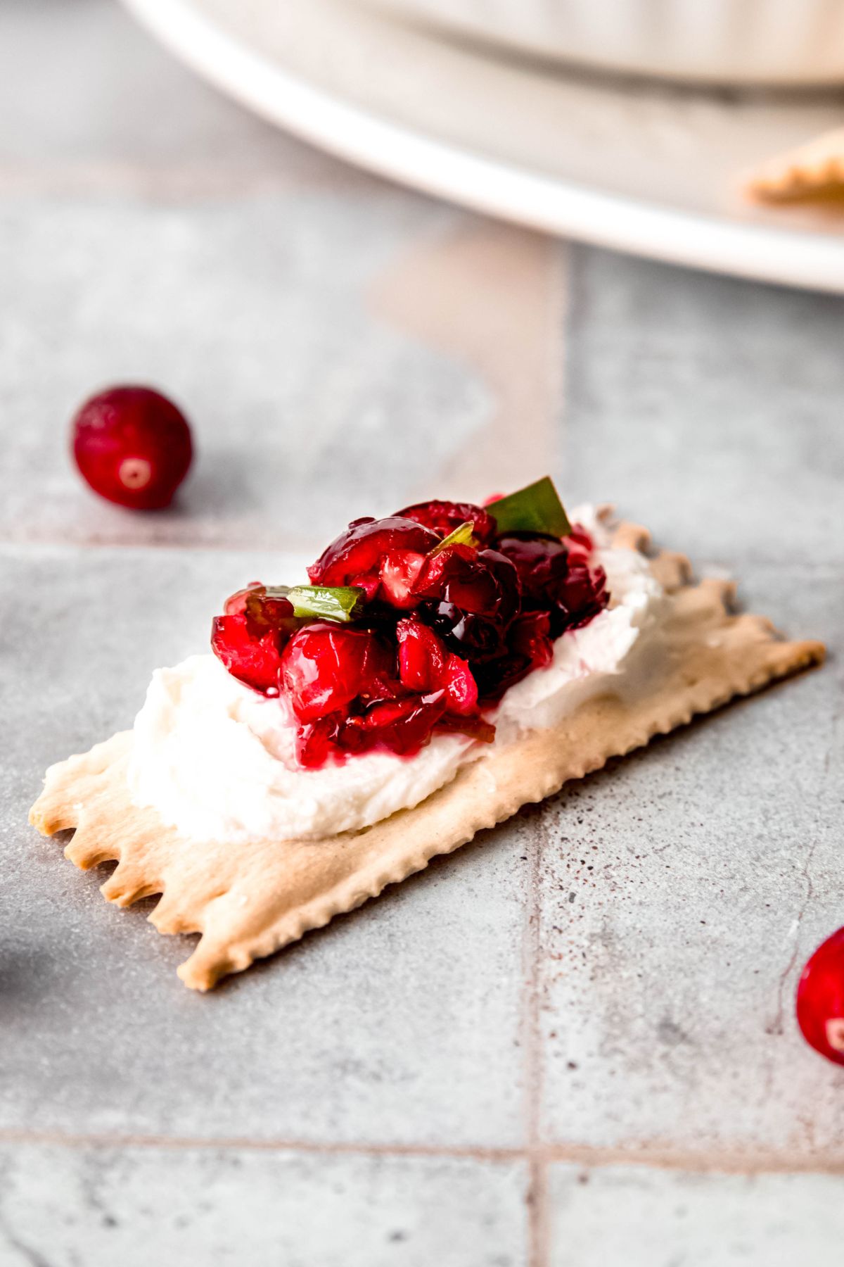 cranberry jalapeno cream cheese dip on a thin rectangular cracker on a grey tile surface.
