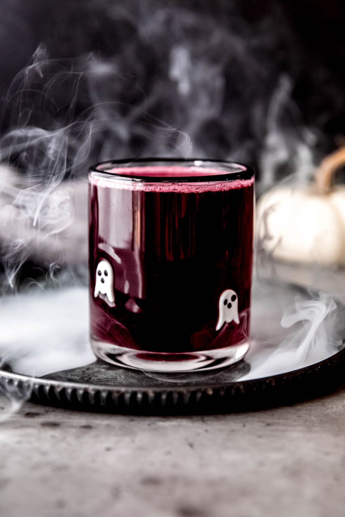 A side shot of a glass of halloween lemonade on a metal tray with fog curling around it.
