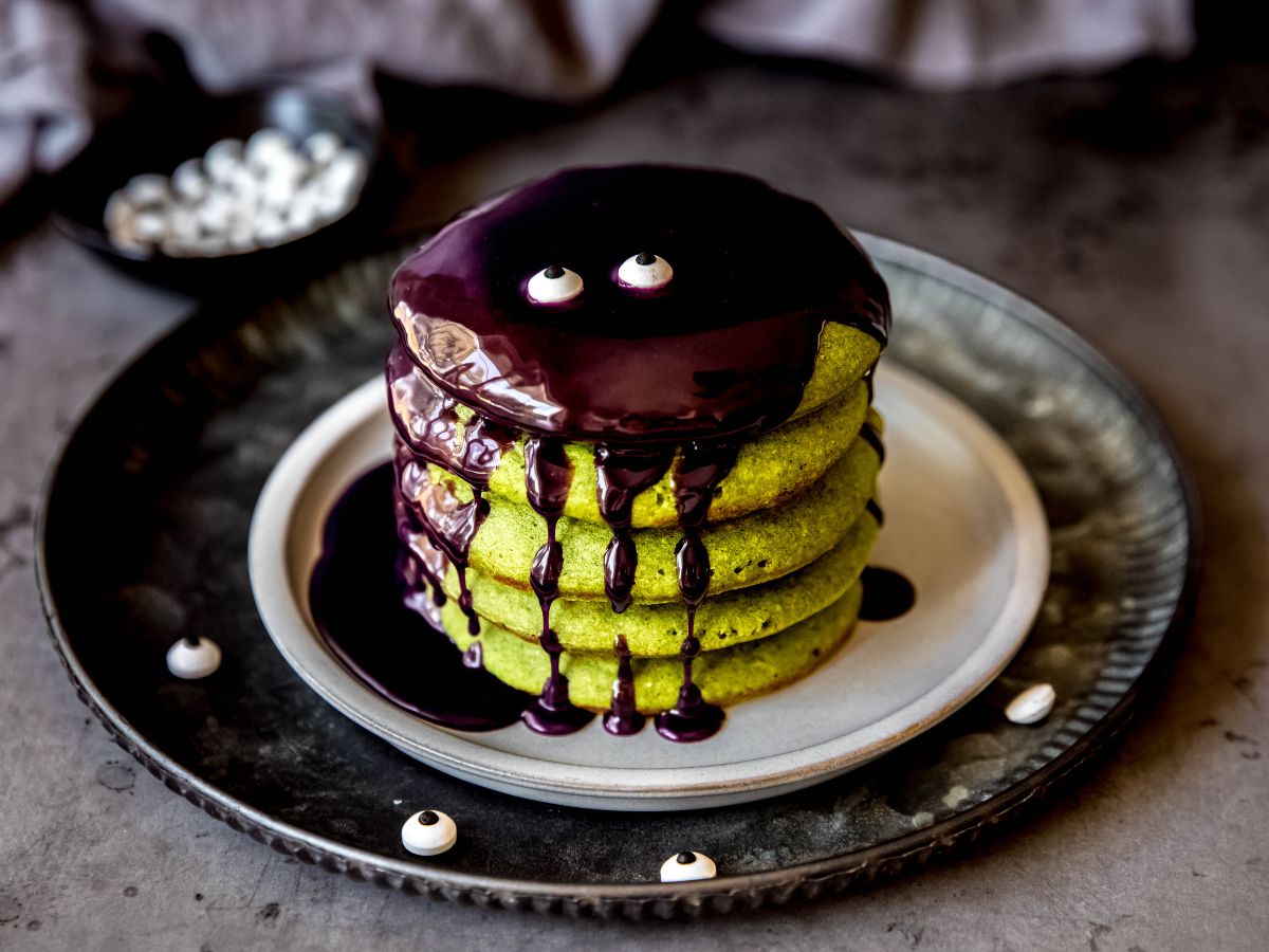 A horizontal shot of a stack of healthy green Halloween pancakes covered with ube sauce for a Halloween breakfast.