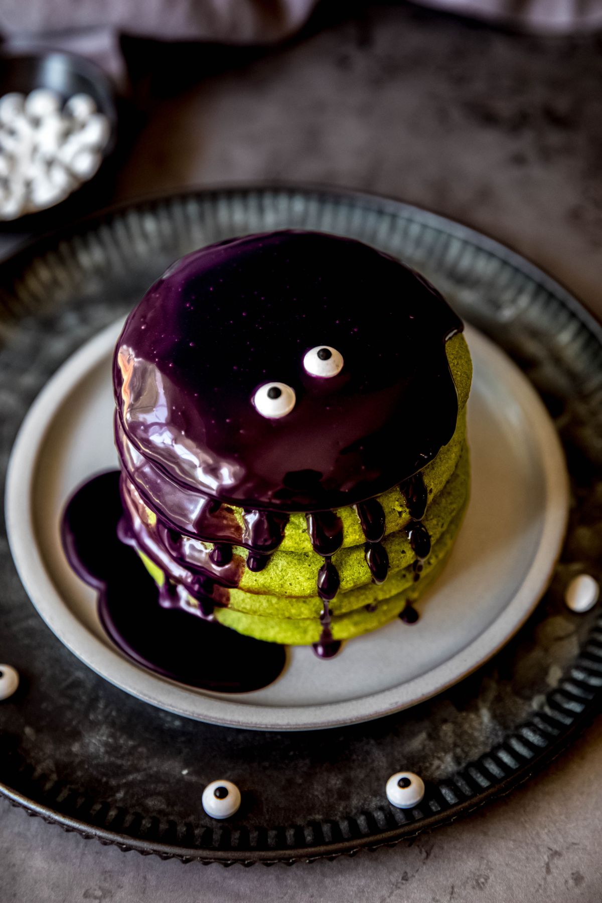 An overhead angled shot of a stack of green spinach pancakes topped with purple ube sauce for halloween.
