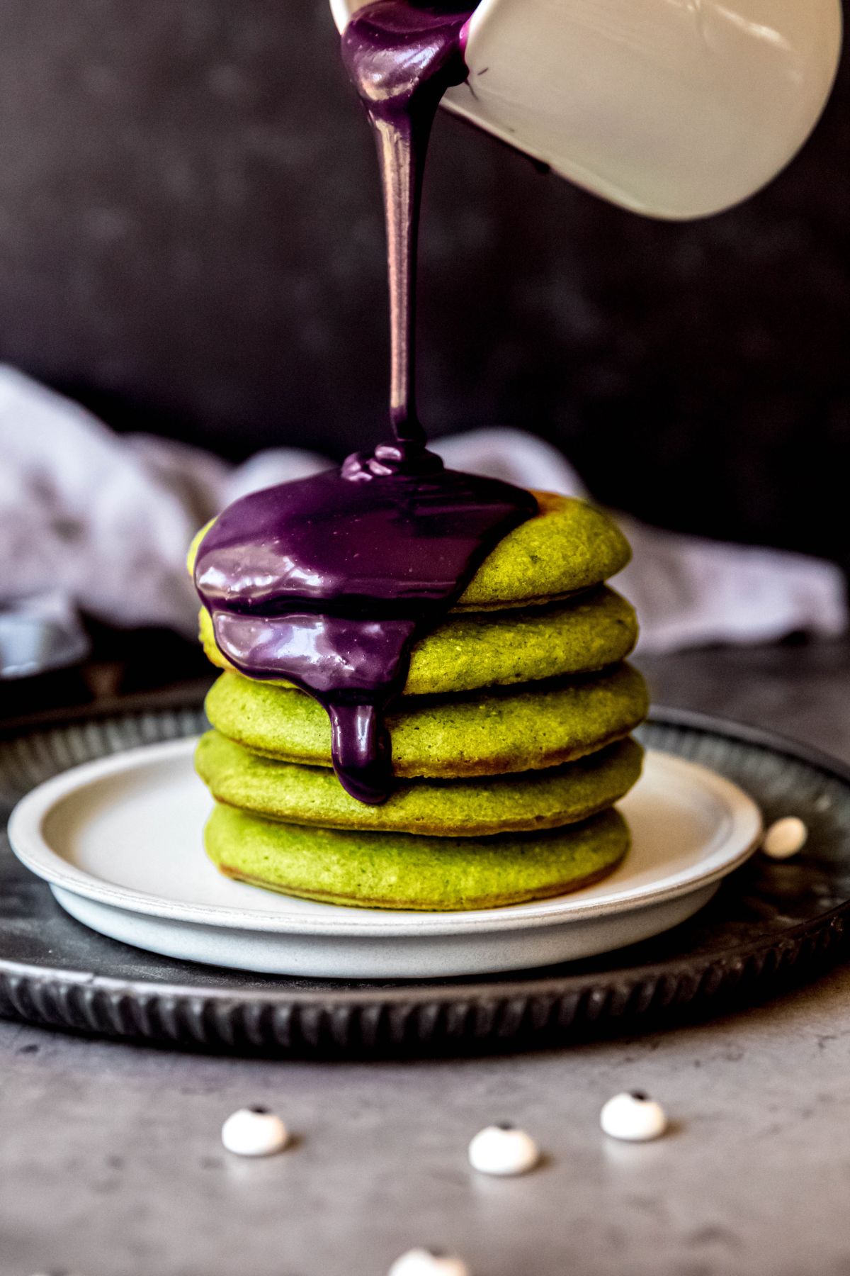 Pouring the ube sauce on top of a stack of green pancakes.