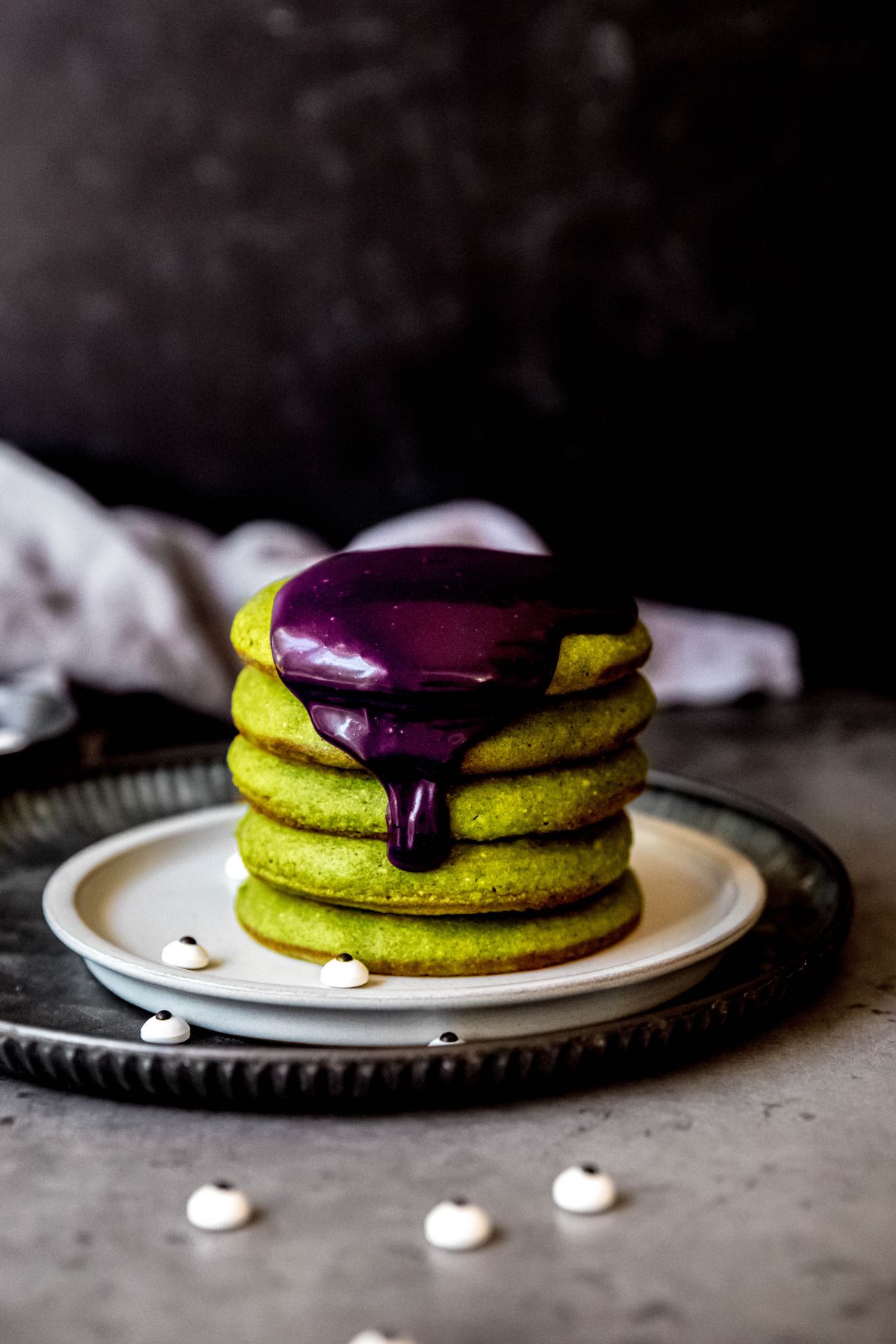 A side shot of a stack of green halloween pancakes with purple ube sauce on top.