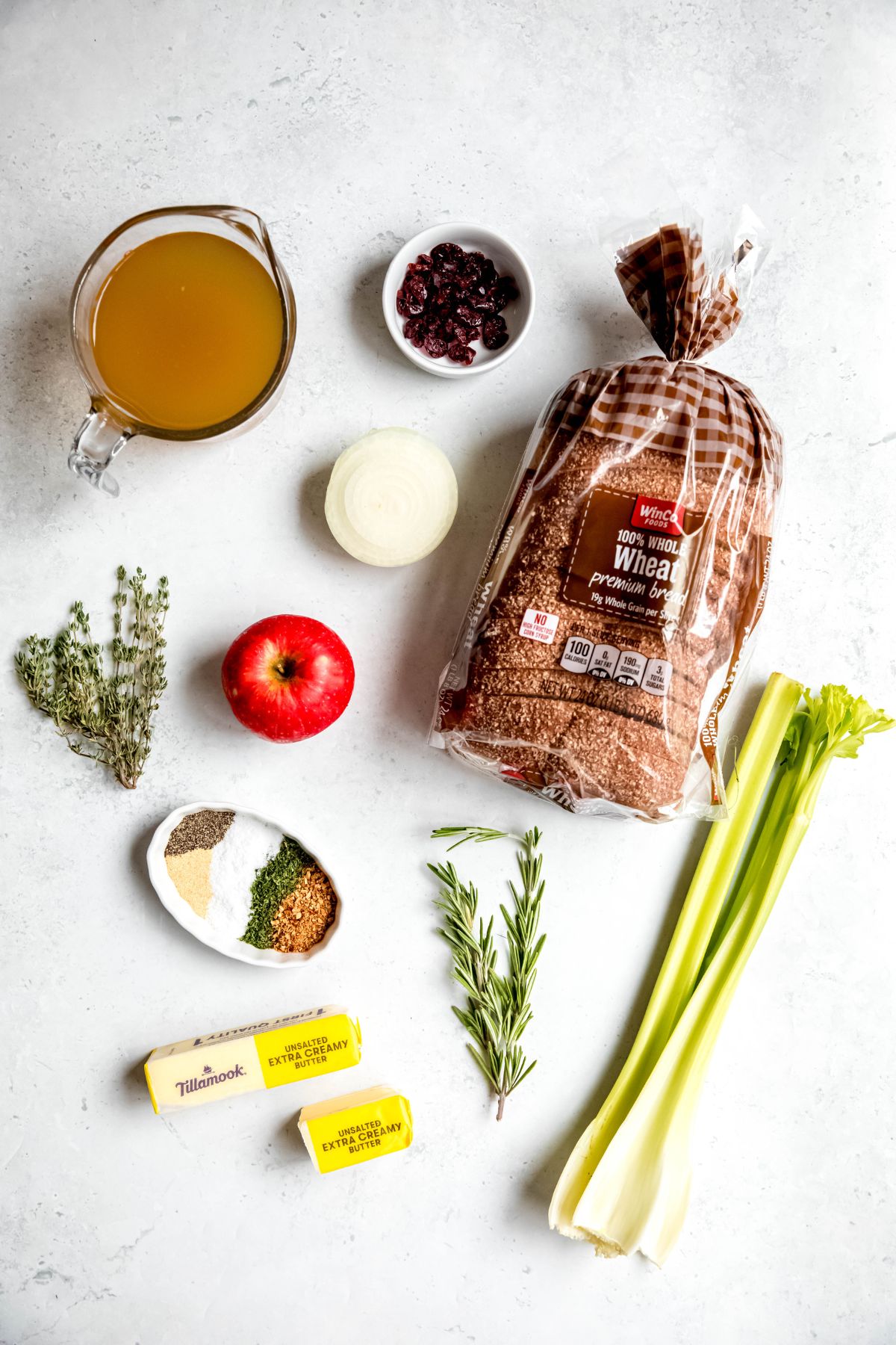 ingredients needed to make make ahead cranberry apple stuffing with whole wheat bread measured out on a white table.