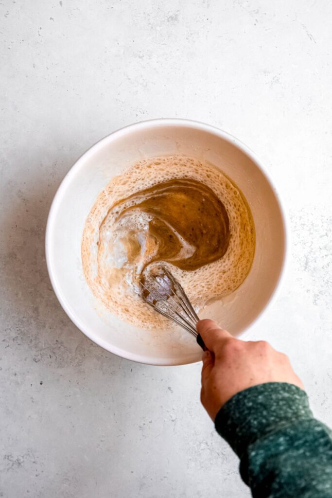 action shot of a hand in a green sweater whisking the wet ingredients together.