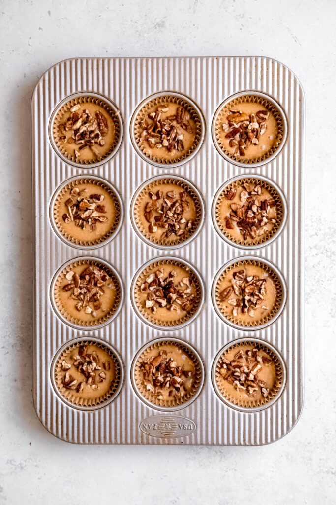 muffin batter divvied up between 12 muffin wells in a tin and sprinkled with the remaining chopped pecans before baking.
