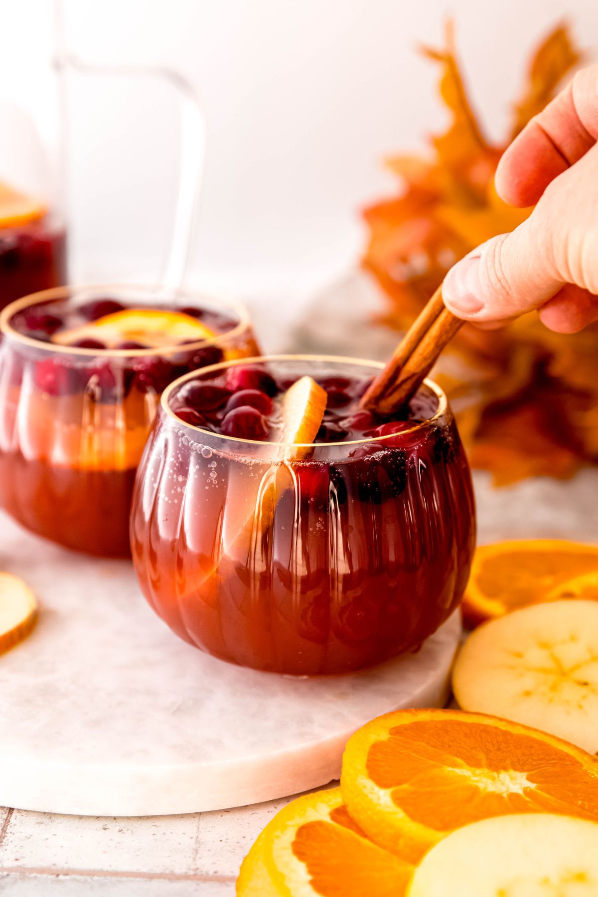 hand placing a cinnamon stick in a glass of Thanksgiving punch for garnish.
