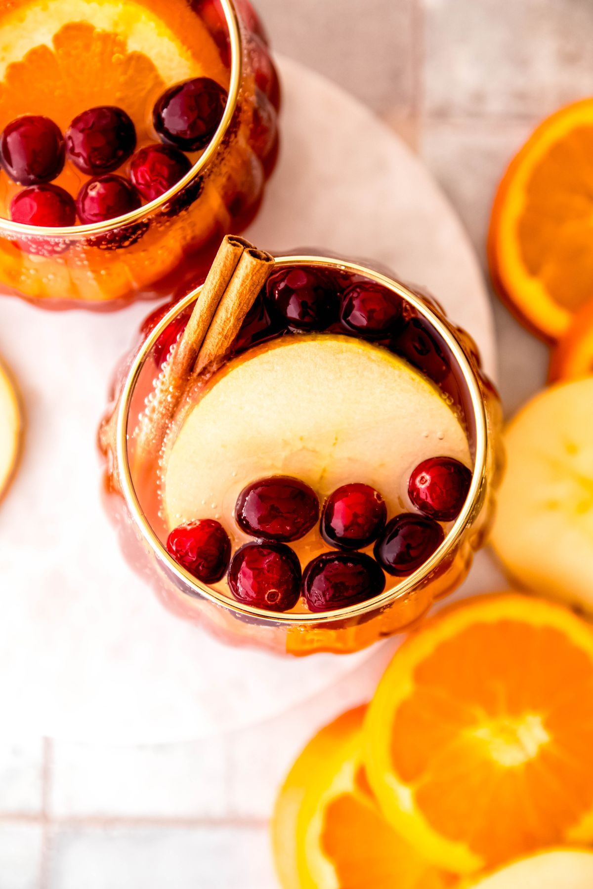 overhead shot looking down into a glass of Thanksgiving punch with a slice of apple, cranberries, and a cinnamon stick floating on top with fresh slices of orange and apple framing the shot beneath.