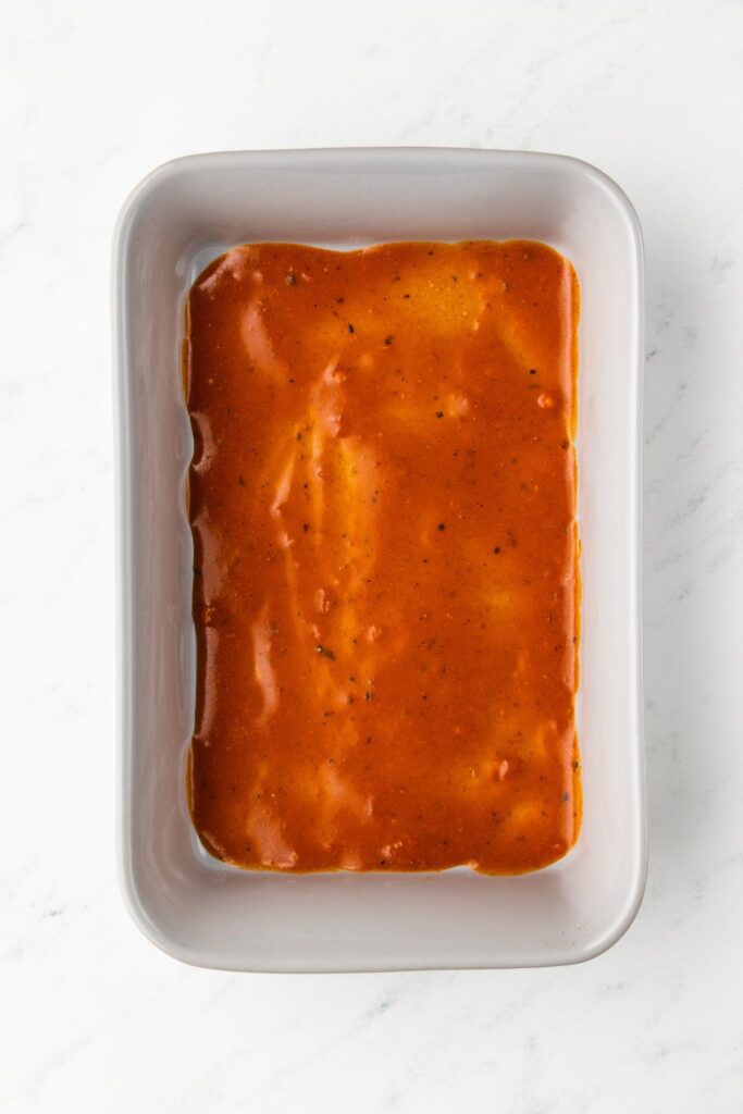 red enchilada sauce added in a thin layer in the bottom of a casserole dish.