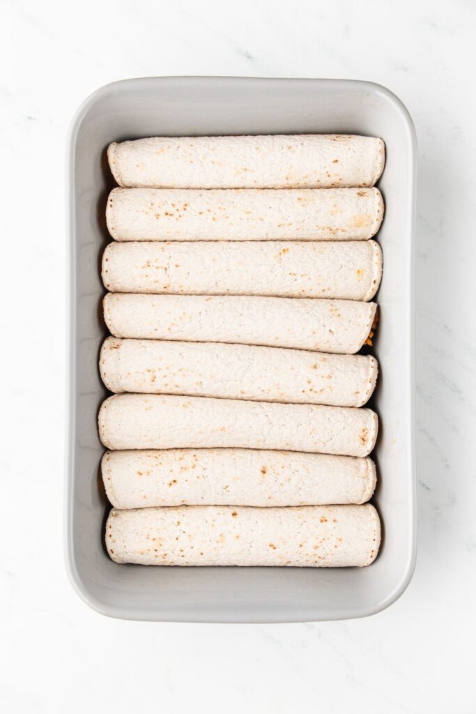 rolled and stuffed turkey enchiladas lined up in a neat row on top of the enchilada sauce.