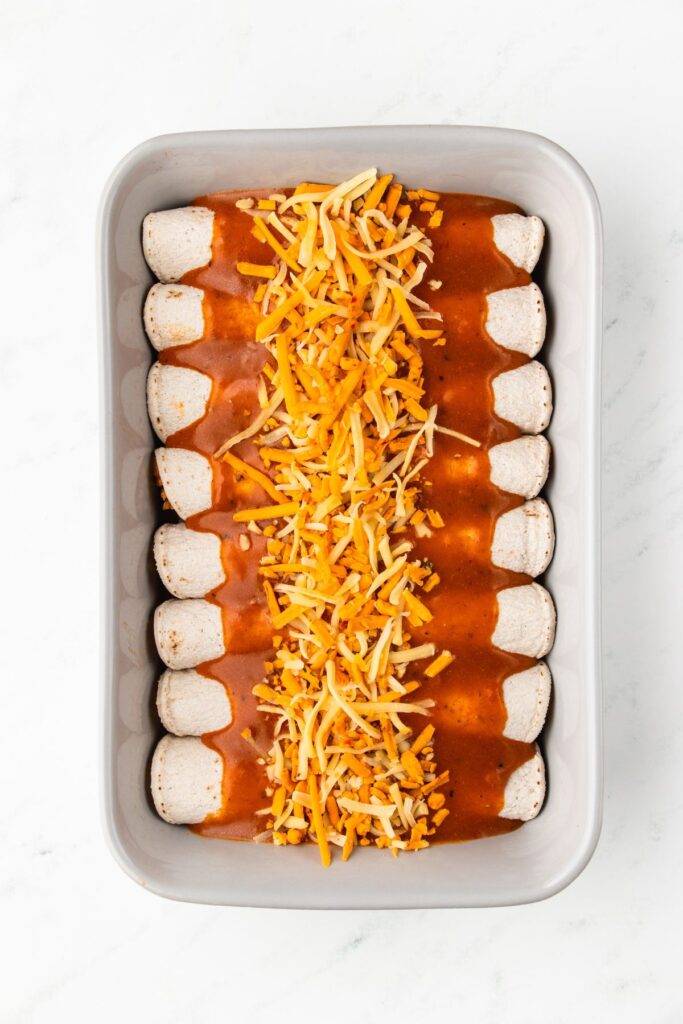 turkey enchiladas topped with extra enchilada sauce and shredded cheese before baking.