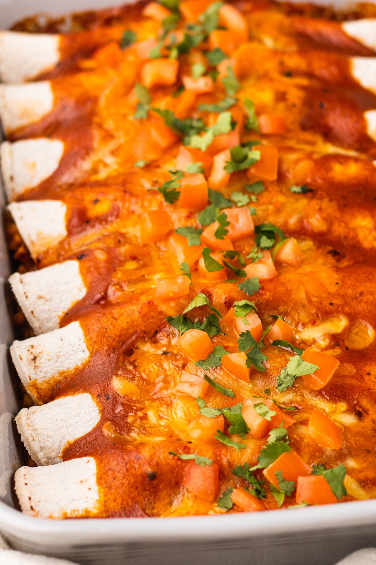 casserole dish filled with baked ground turkey enchiladas topped with fresh pico de gallo and chopped cilantro.