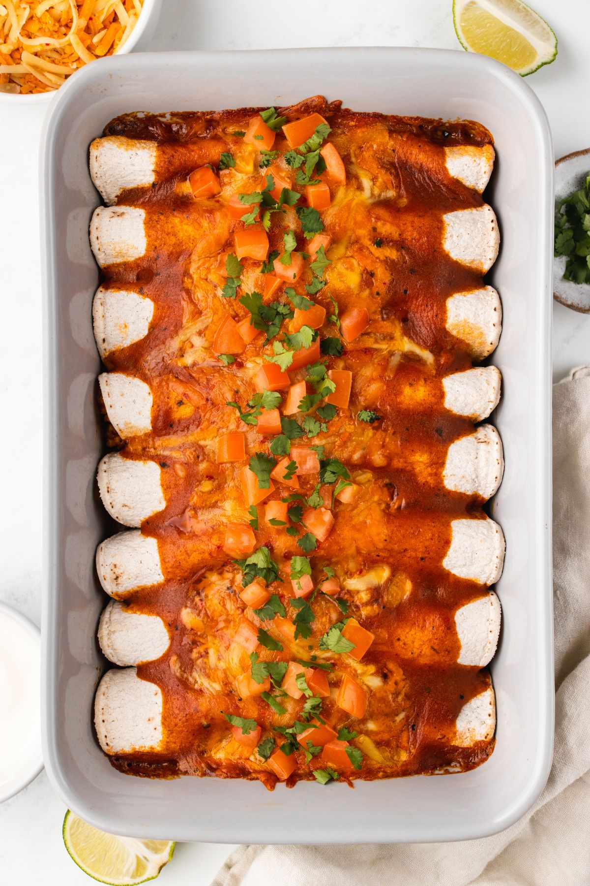 overhead closeup shot of a 9x13 of baked turkey enchiladas with red sauce, tomatoes, and cilantro.