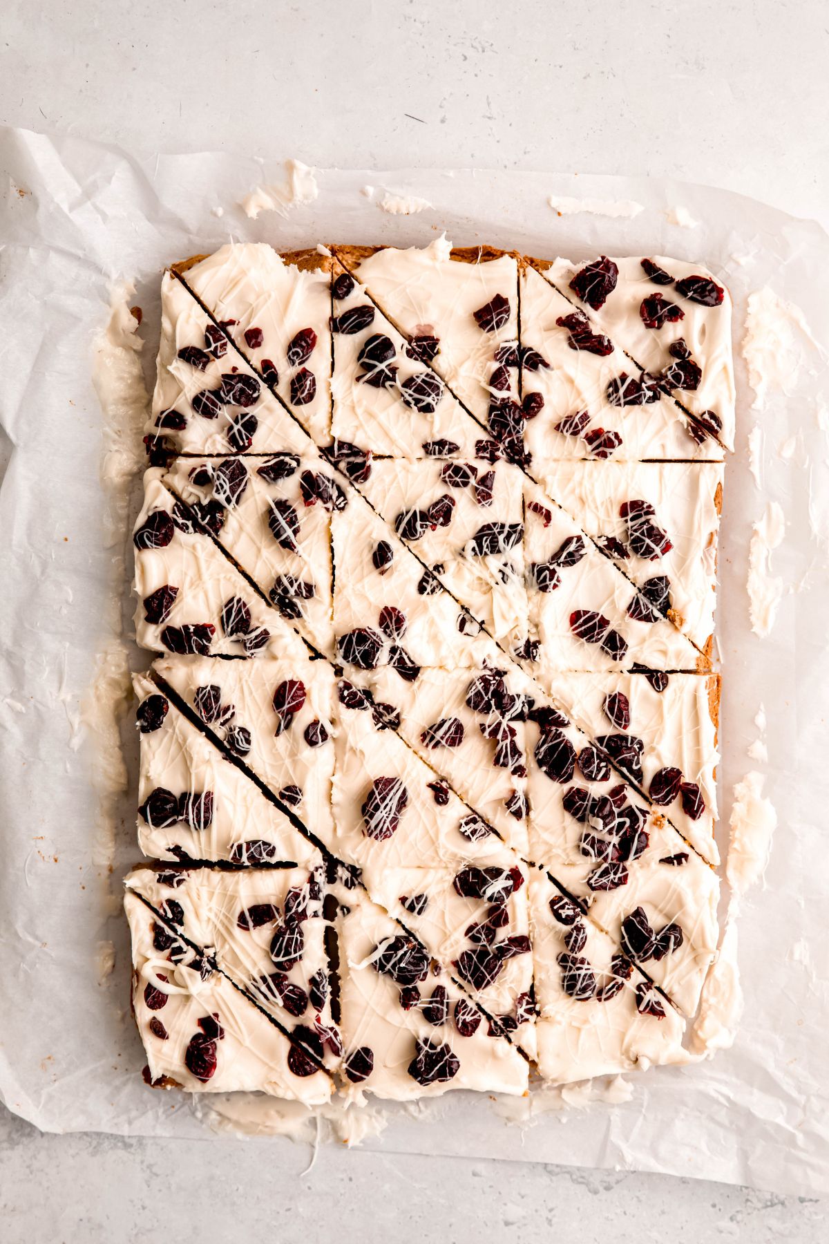 parchment paper with the batch of whole wheat cranberry bliss bars that have been cut into 24 triangles.