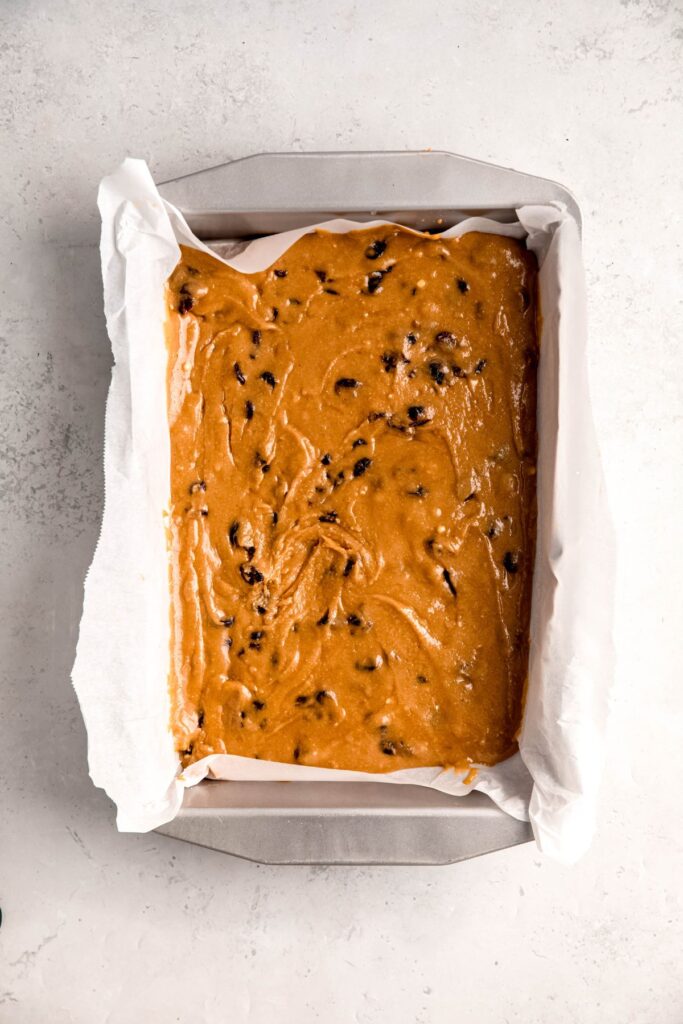 cranberry white chocolate blondie batter spread out in a parchment lined 9x13 pan.