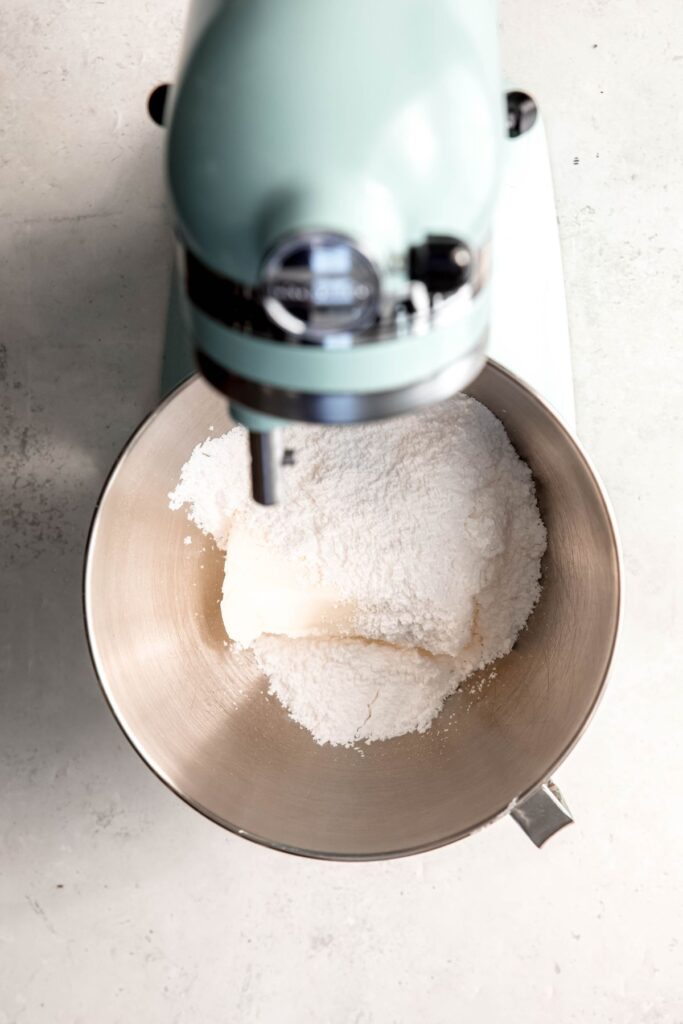 stand mixer with powdered sugar and a block of cream cheese in the bowl.
