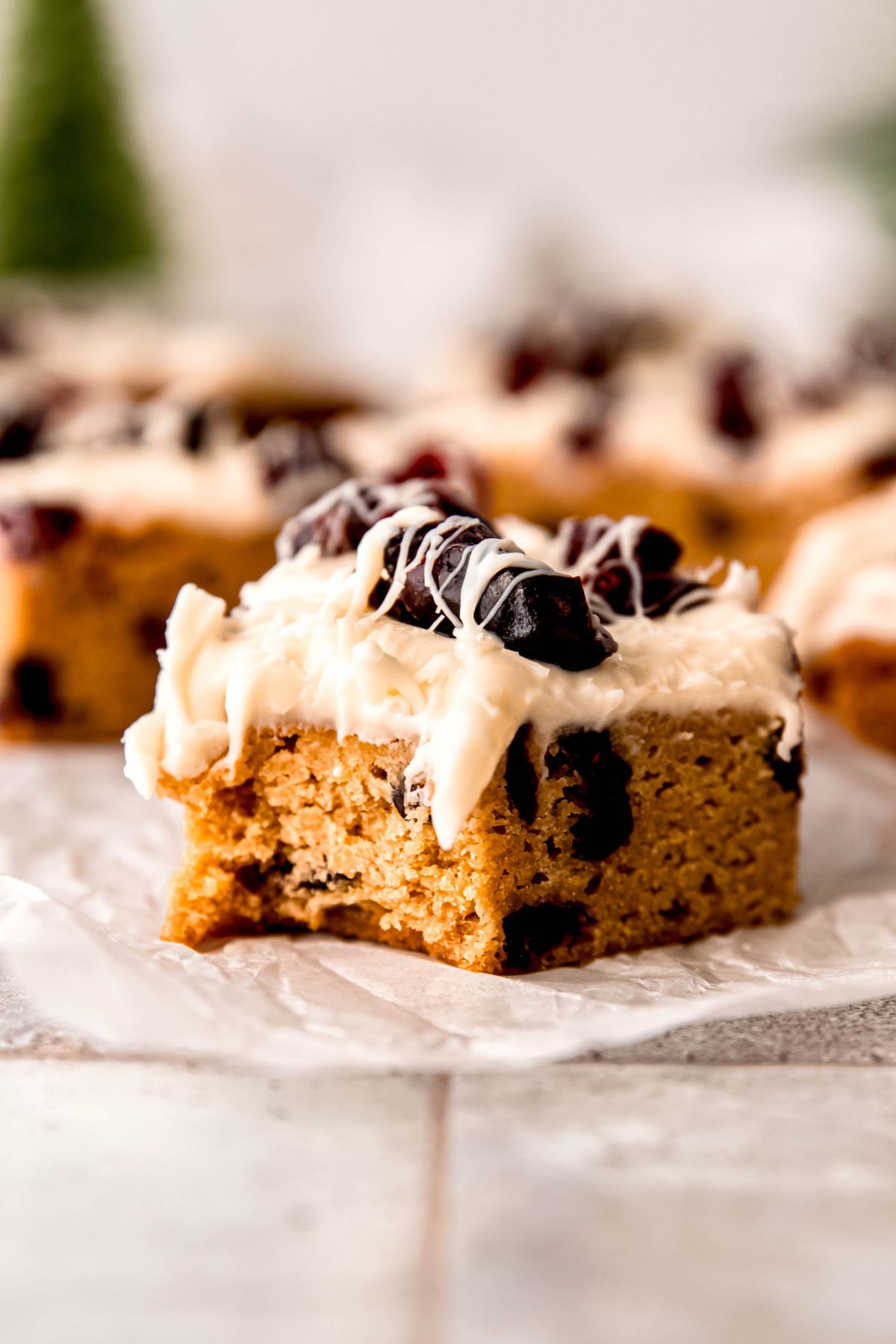 side on view of a copycat whole wheat Starbucks cranberry bliss bar with a bite taken out showing the thick blondie base studded with dried cranberries and the layered frosting top.