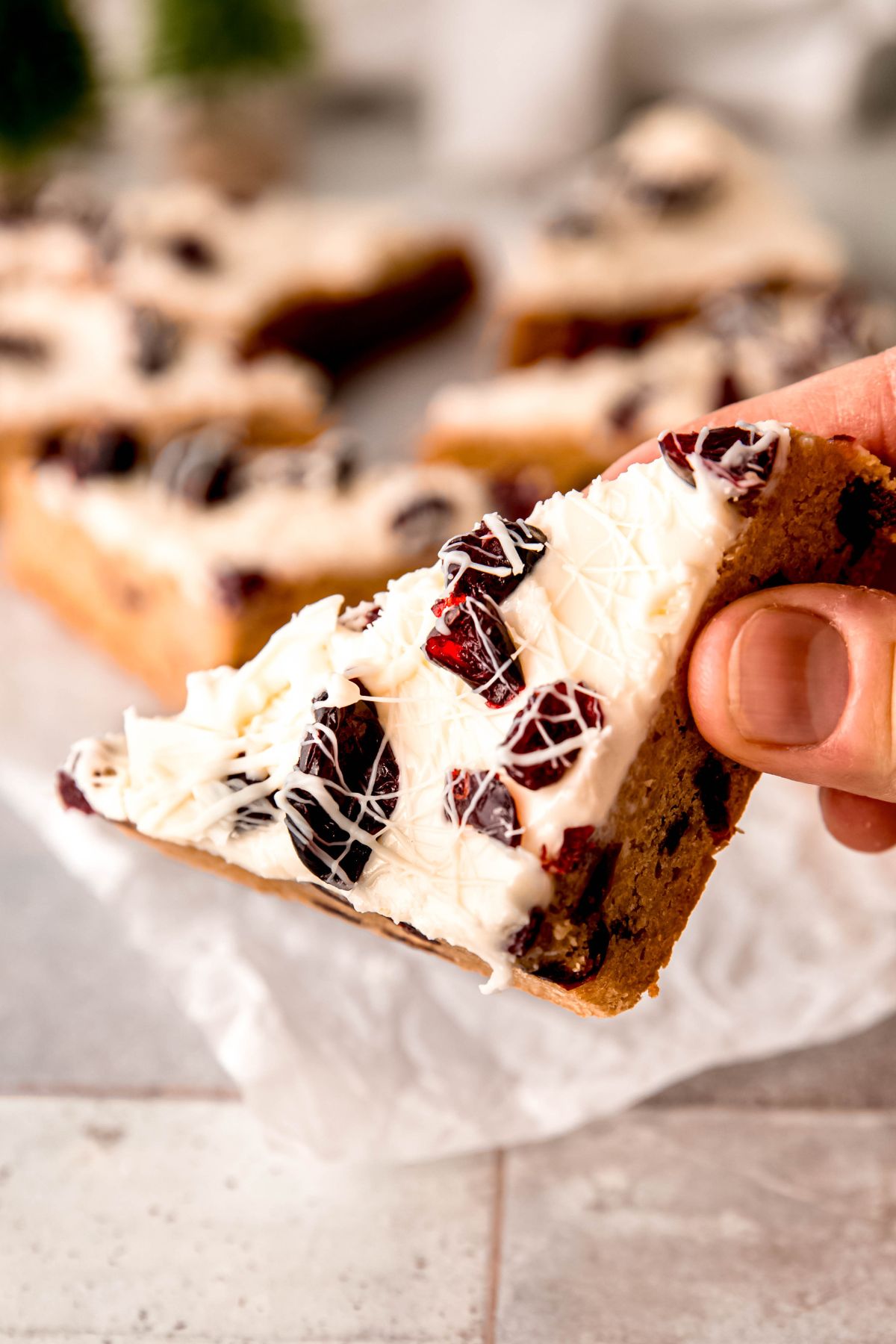 hand holding a single copycat cranberry bliss bar with the frosting side facing the camera showing the chewy cranberries and white chocolate drizzle.